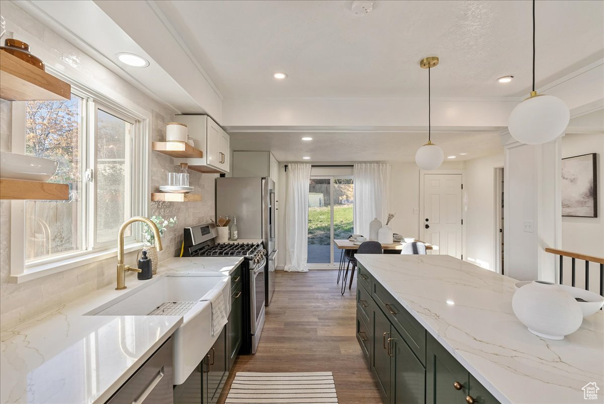 Kitchen featuring dark wood-type flooring, decorative backsplash, hanging light fixtures, stainless steel gas stove, and light stone countertops