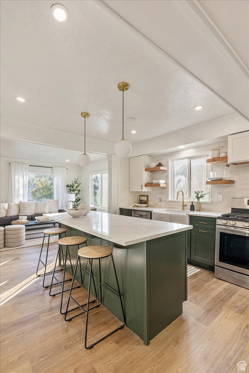 Kitchen featuring white cabinetry, stainless steel stove, green cabinetry, hanging light fixtures, and light hardwood / wood-style floors