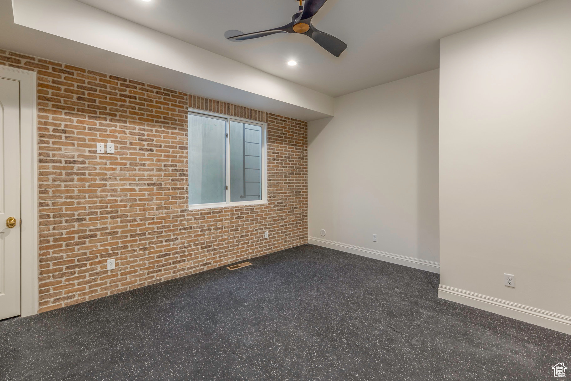 Spare room featuring ceiling fan, brick wall, and dark colored carpet