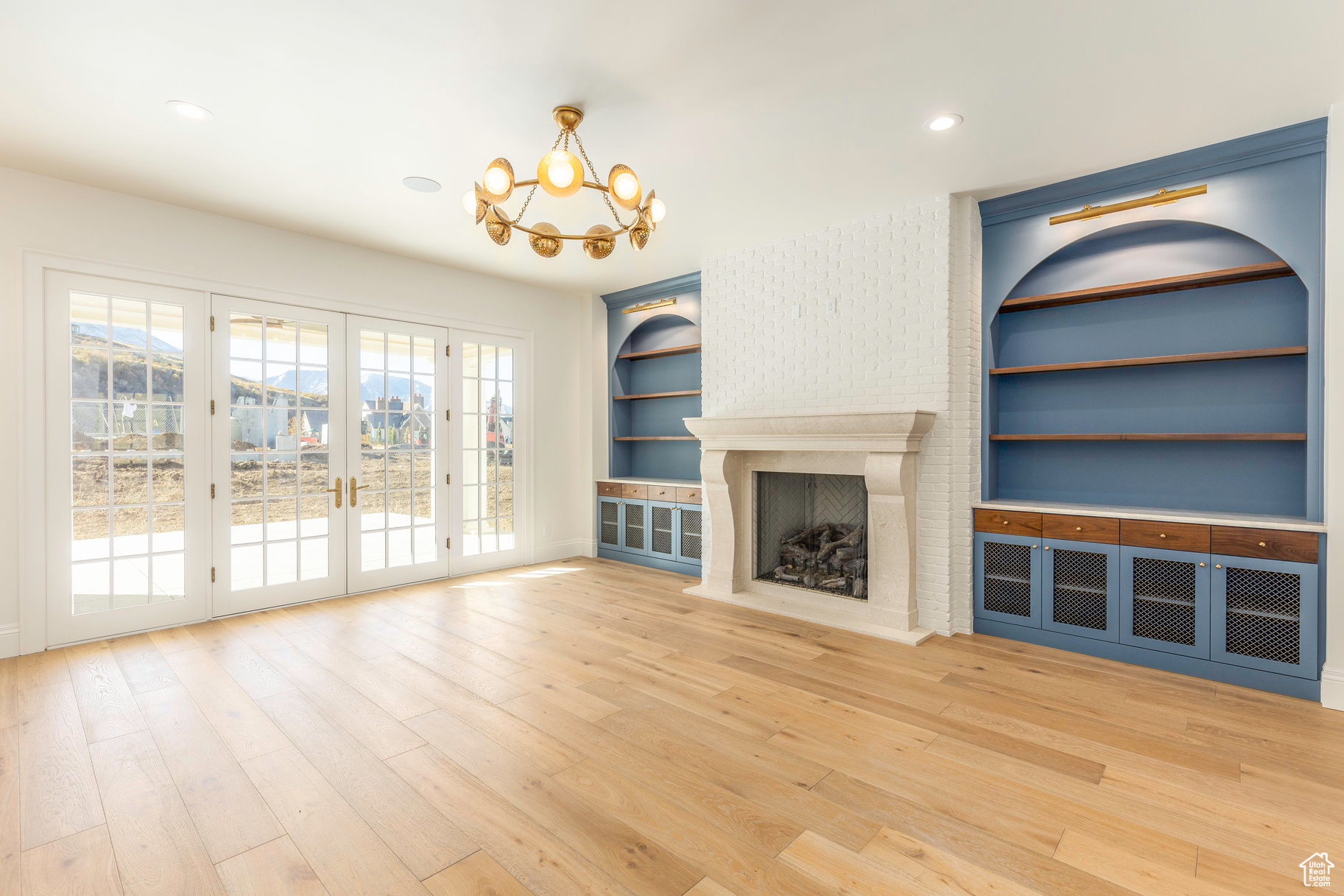 Unfurnished living room featuring french doors, an inviting chandelier, hardwood / wood-style flooring, a premium fireplace, and built in features