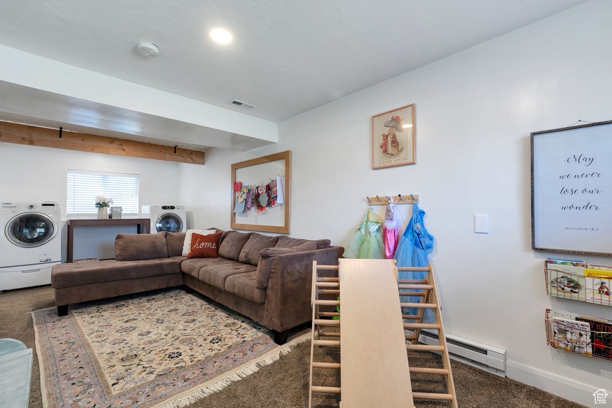 Carpeted living room featuring beam ceiling, baseboard heating, and washer / dryer