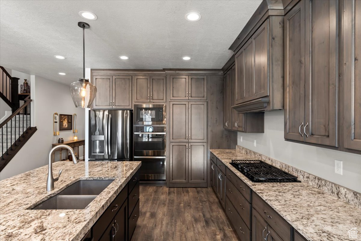 Kitchen featuring sink, hanging light fixtures, dark hardwood / wood-style flooring, dark brown cabinetry, and stainless steel appliances