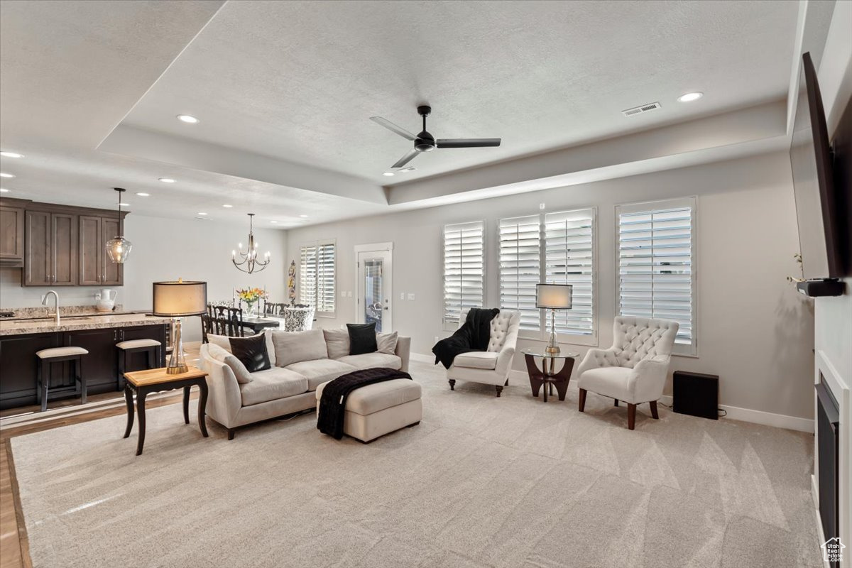 Living room featuring light carpet, a textured ceiling, ceiling fan with notable chandelier, and sink