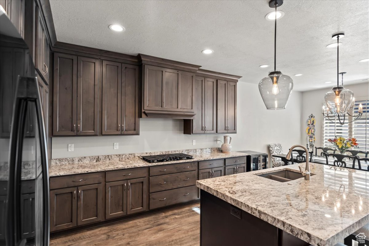 Kitchen featuring dark brown cabinetry, black appliances, sink, hardwood / wood-style floors, and hanging light fixtures