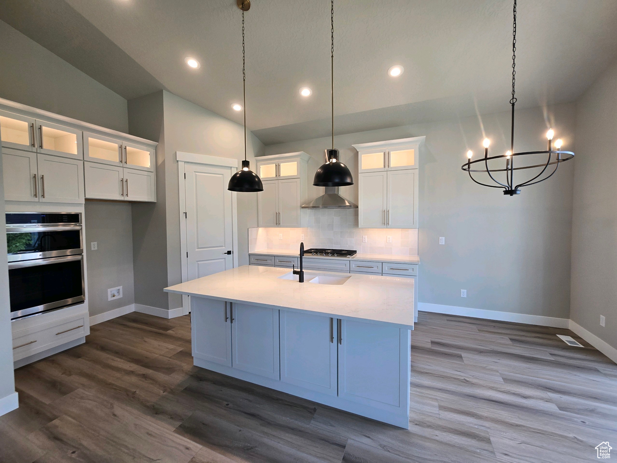 Kitchen with white cabinets, a center island with sink, decorative light fixtures, and appliances with stainless steel finishes