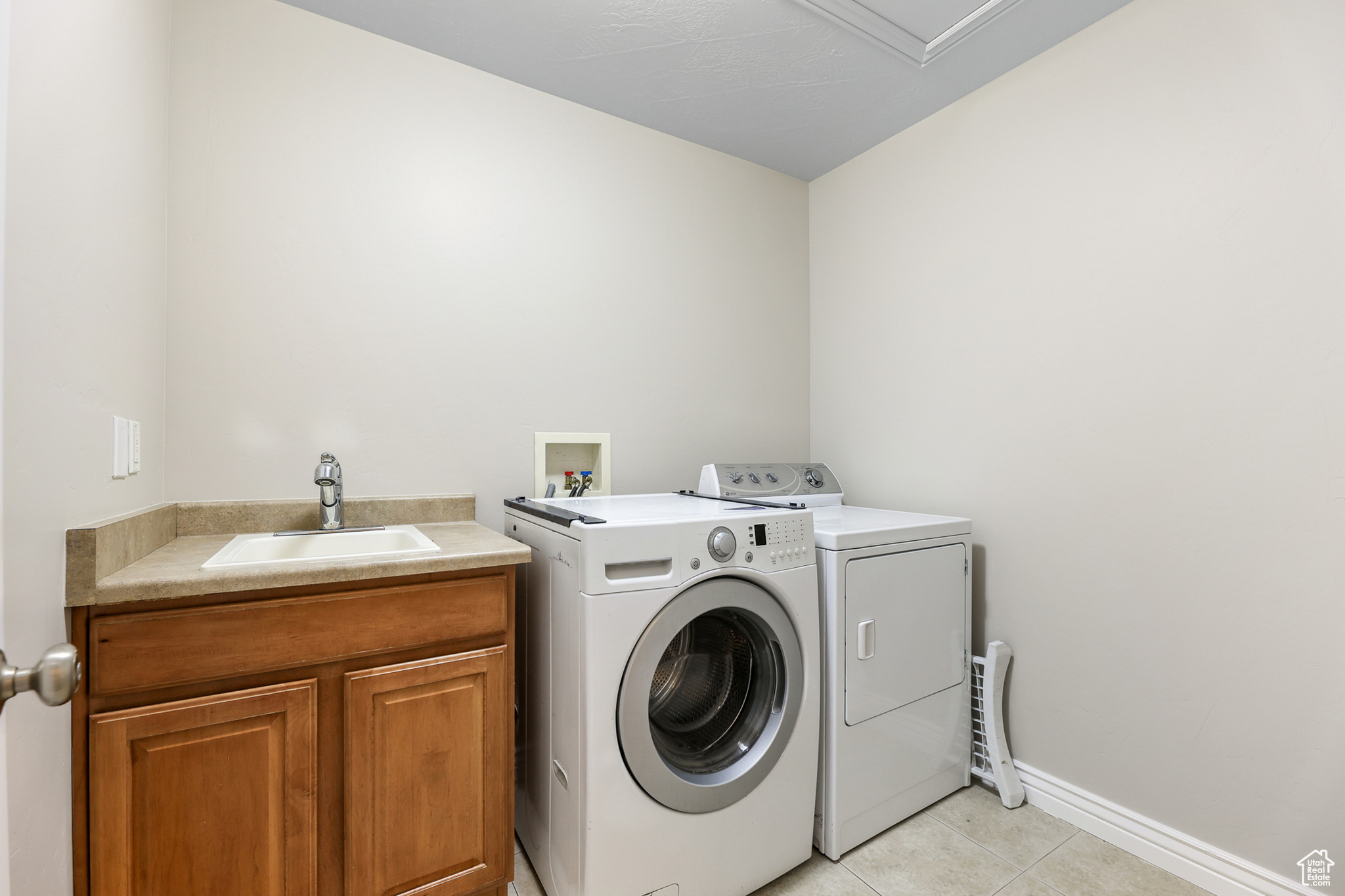 Clothes washing area with cabinets, sink, independent washer and dryer, and light tile patterned floors