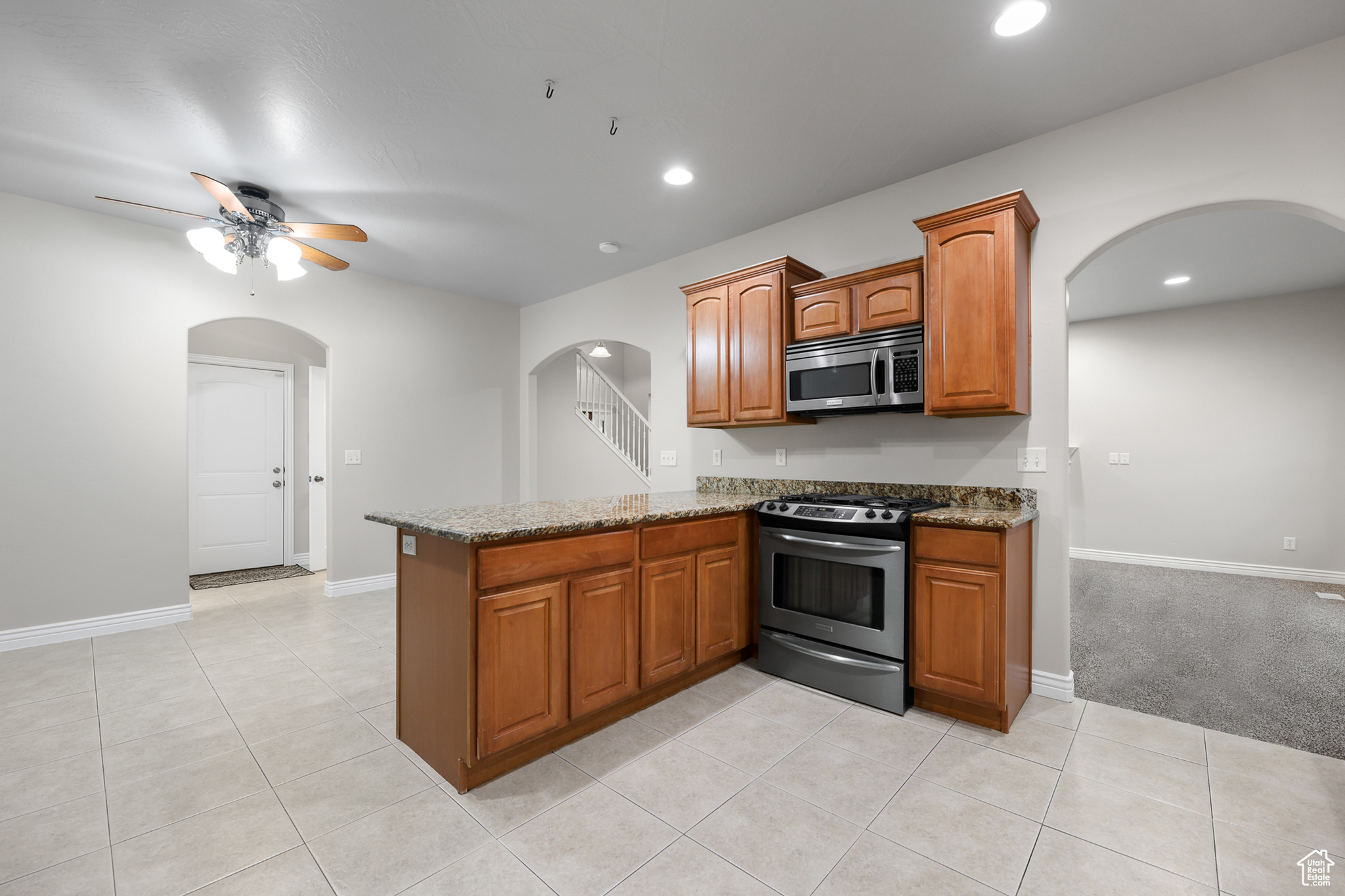 Kitchen featuring stainless steel appliances, light tile patterned floors, stone counters, kitchen peninsula, and ceiling fan