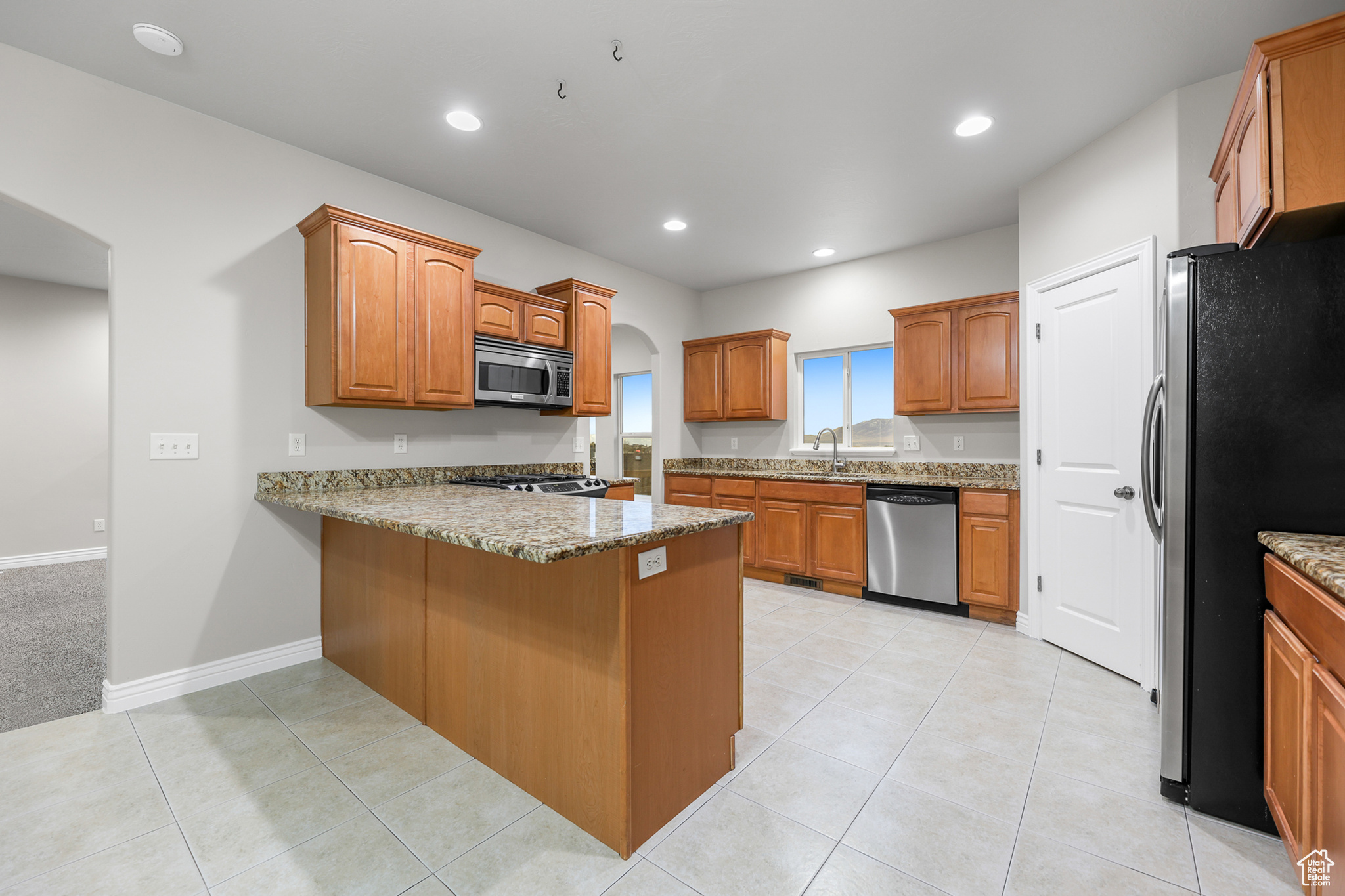 Kitchen featuring appliances with stainless steel finishes, light tile patterned floors, light stone countertops, sink, and kitchen peninsula