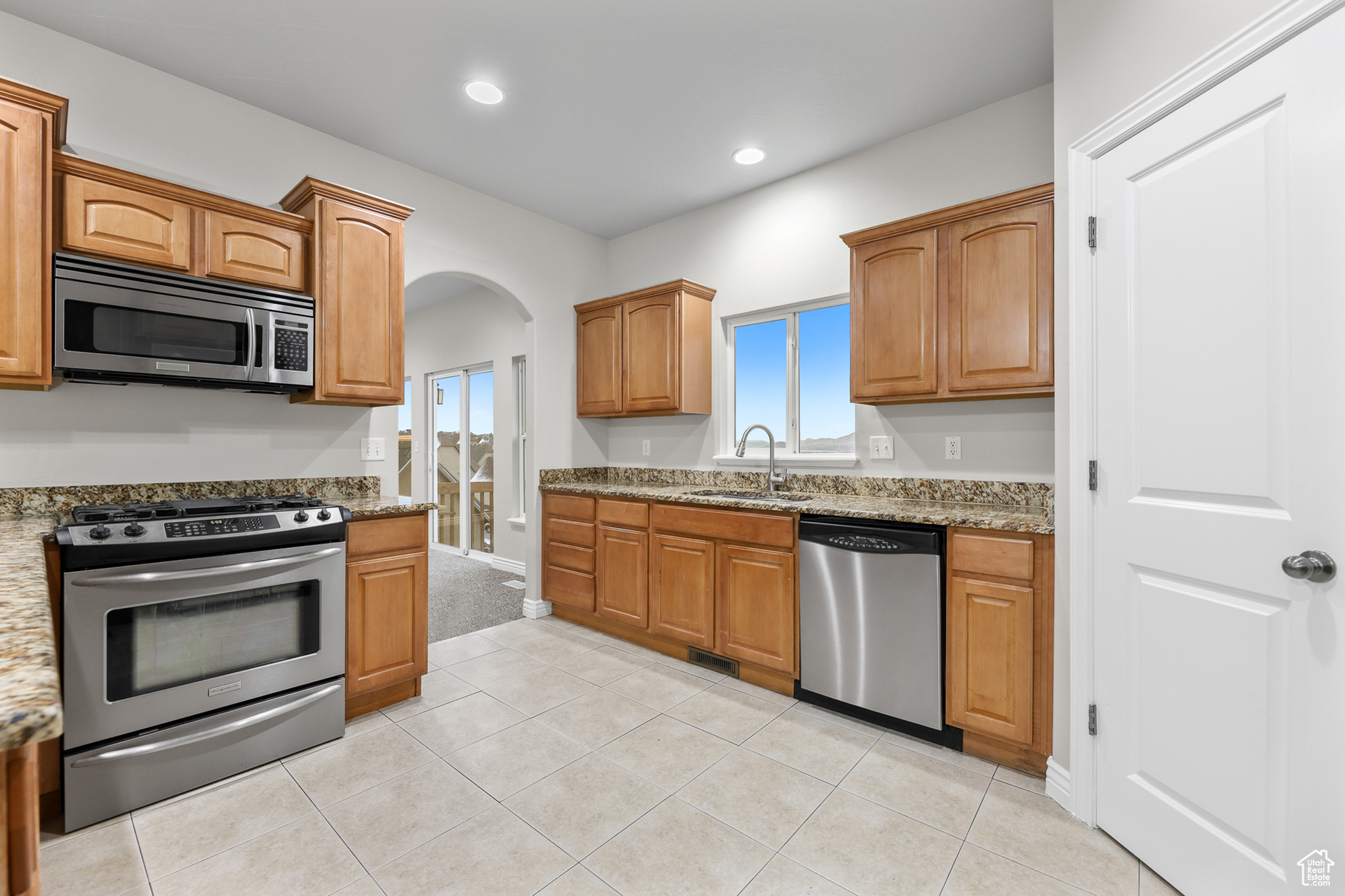 Kitchen featuring light tile patterned flooring, appliances with stainless steel finishes, sink, and light stone countertops