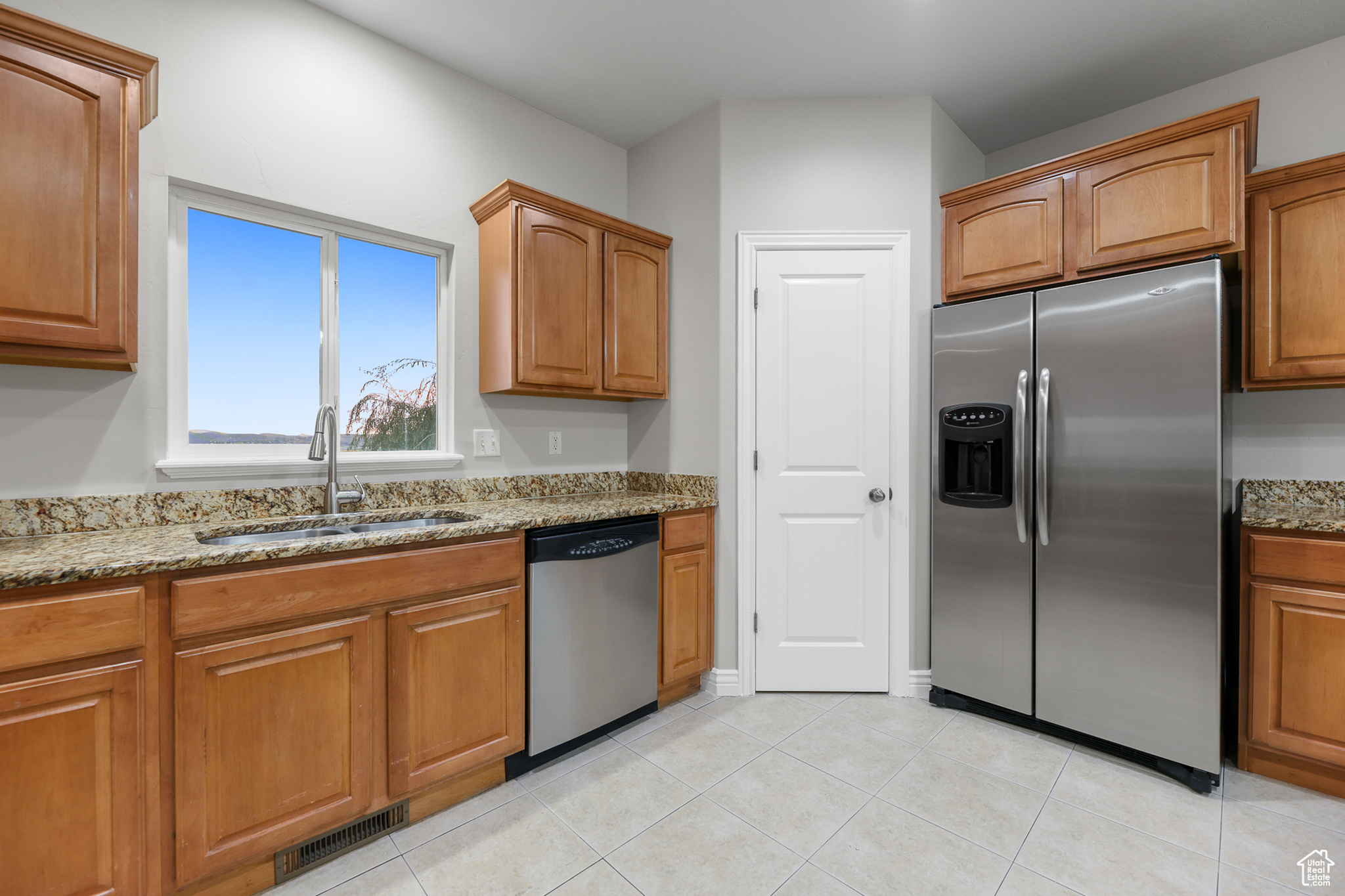 Kitchen featuring appliances with stainless steel finishes, sink, light stone counters, and light tile patterned floors