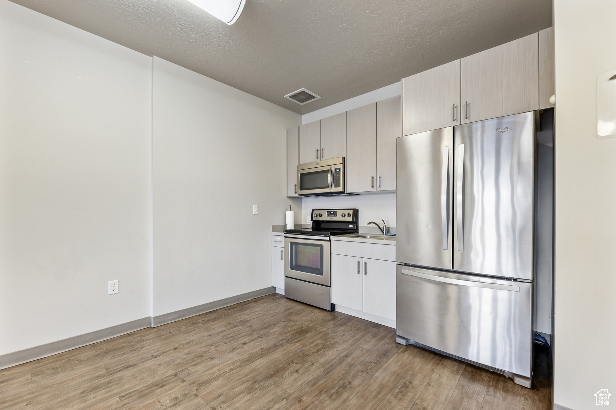 Clubhouse kitchen with sink, appliances with stainless steel finishes, a textured ceiling, and light hardwood / wood-style floors