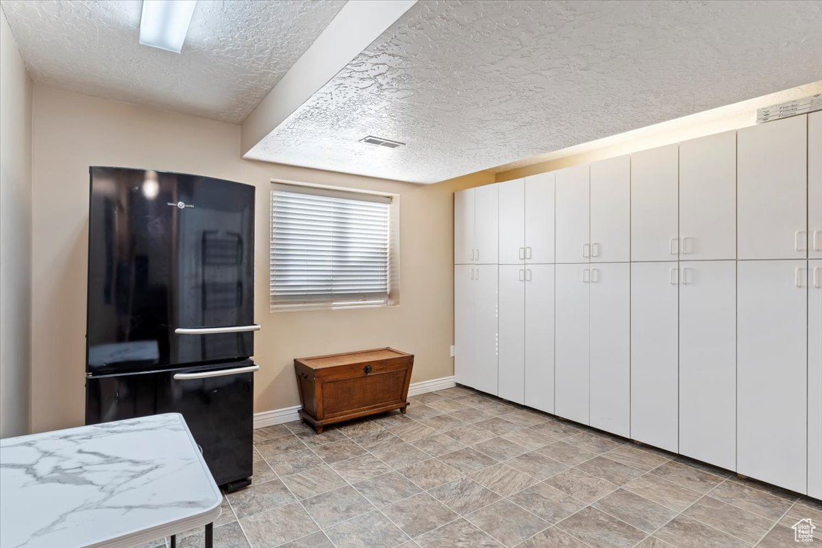 Kitchen with black refrigerator, white cabinetry, and a textured ceiling