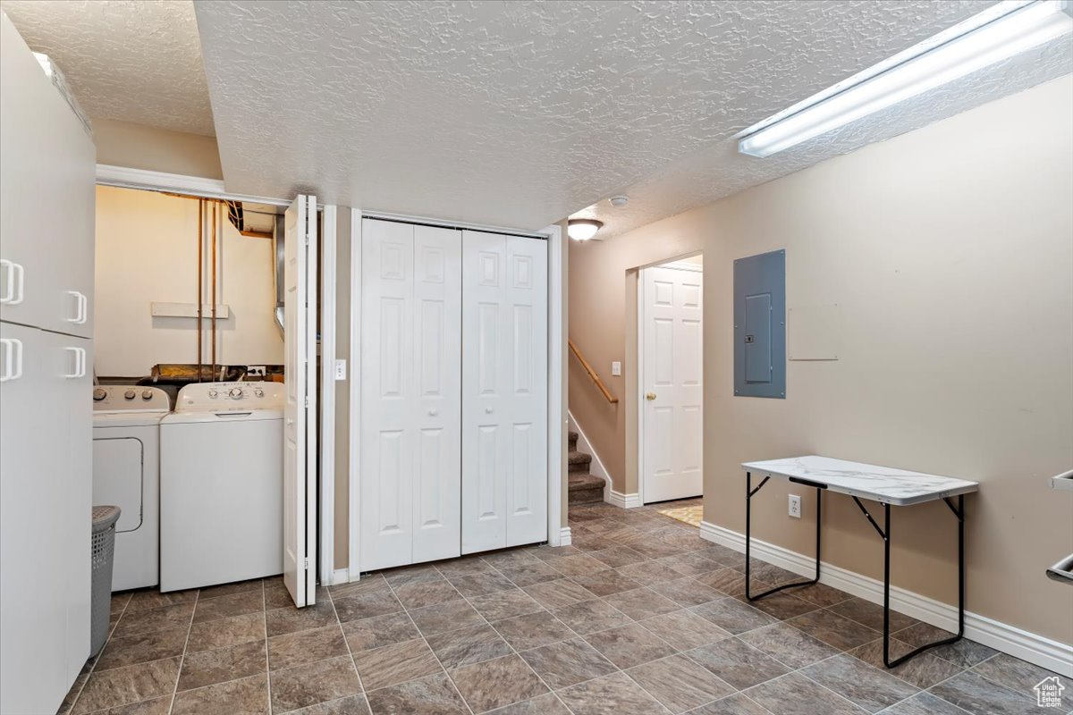 Washroom with electric panel, washing machine and clothes dryer, and a textured ceiling