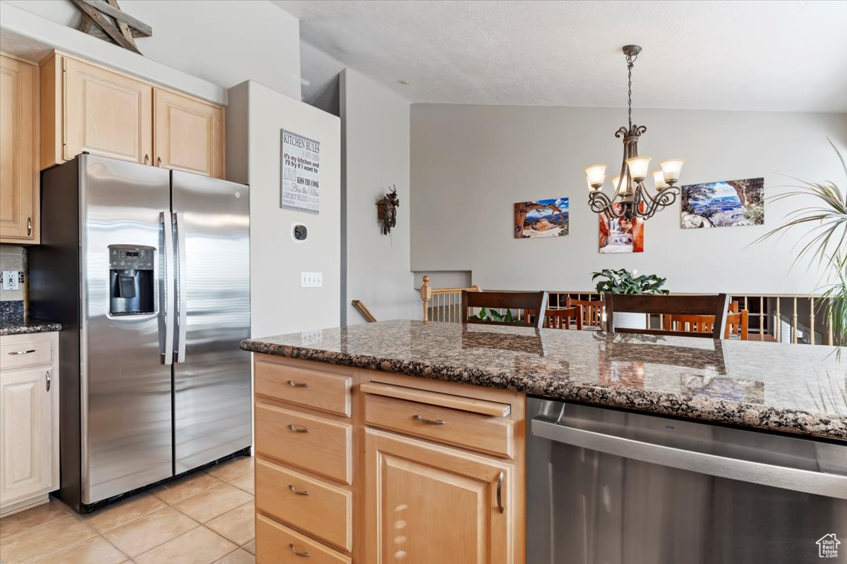 Kitchen featuring stainless steel appliances, vaulted ceiling, light tile patterned flooring, light brown cabinets, and decorative light fixtures