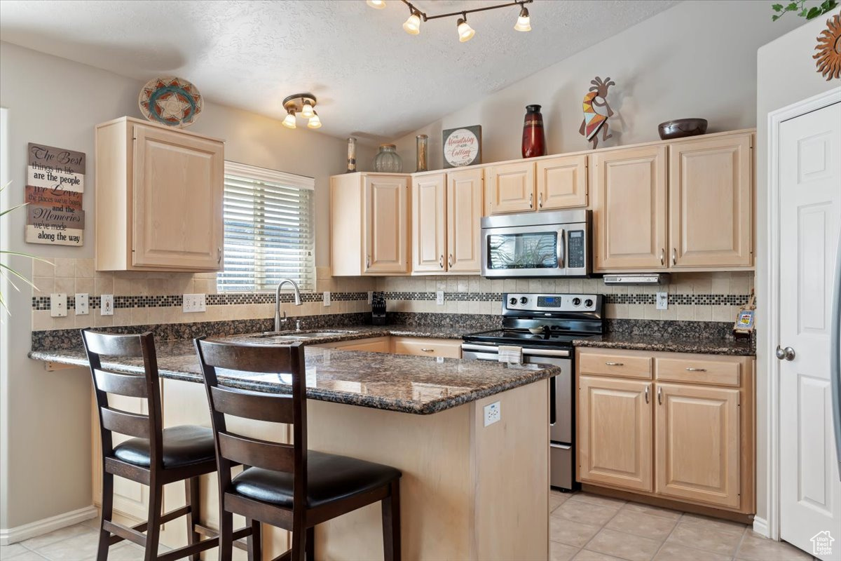 Kitchen with decorative backsplash, appliances with stainless steel finishes, sink, and a breakfast bar area