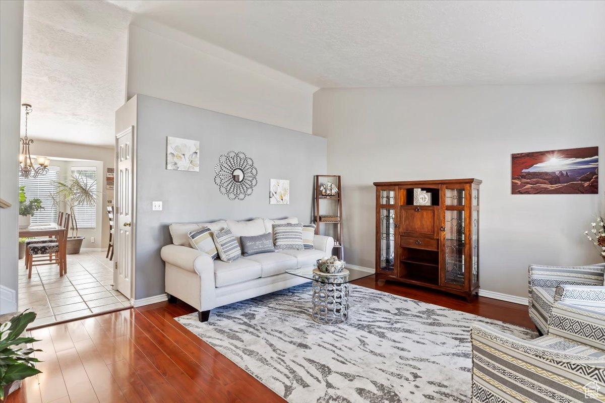 Living room with lofted ceiling, an inviting chandelier, and hardwood / wood-style flooring