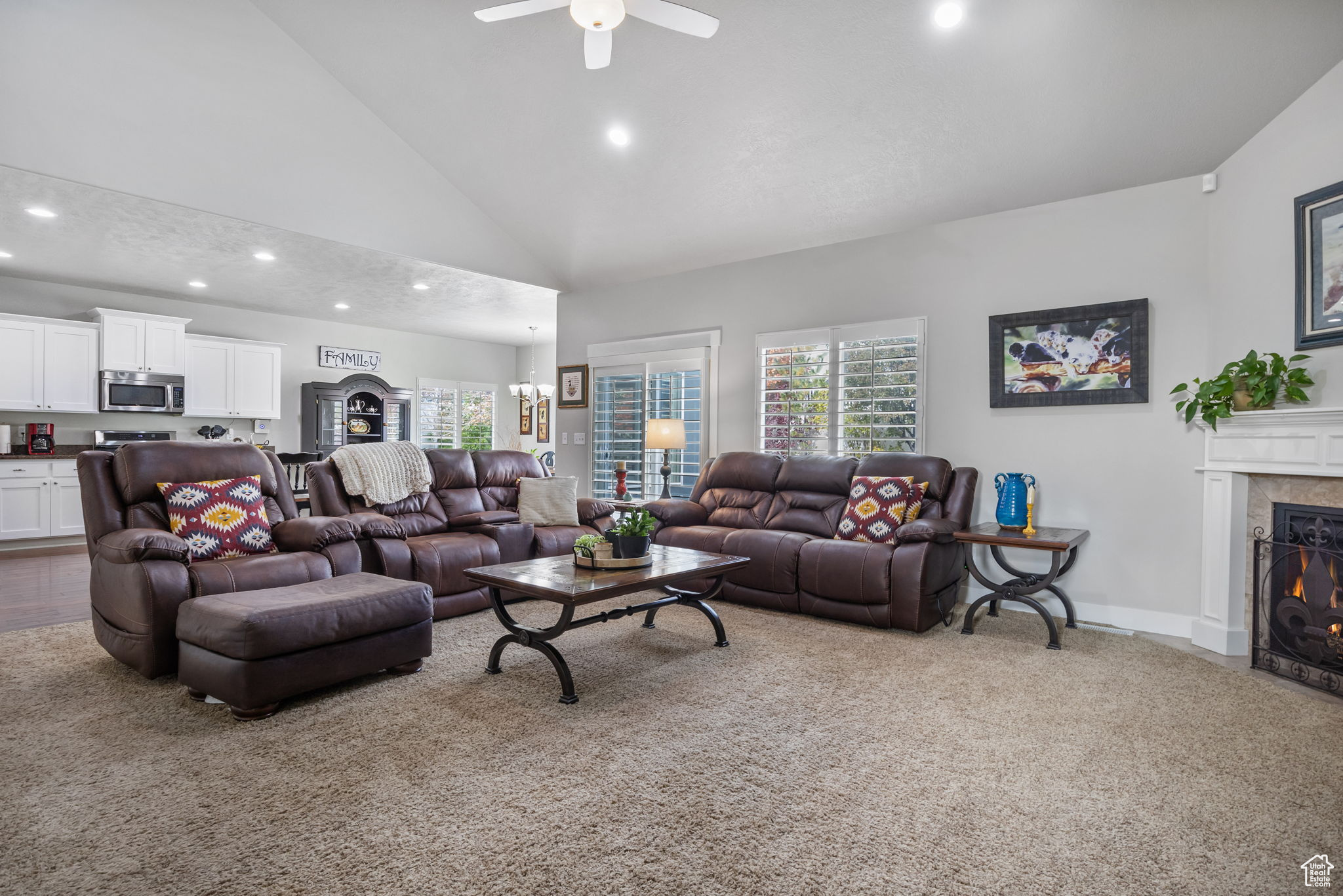 Carpeted living room with ceiling fan with notable chandelier, high vaulted ceiling, and a healthy amount of sunlight