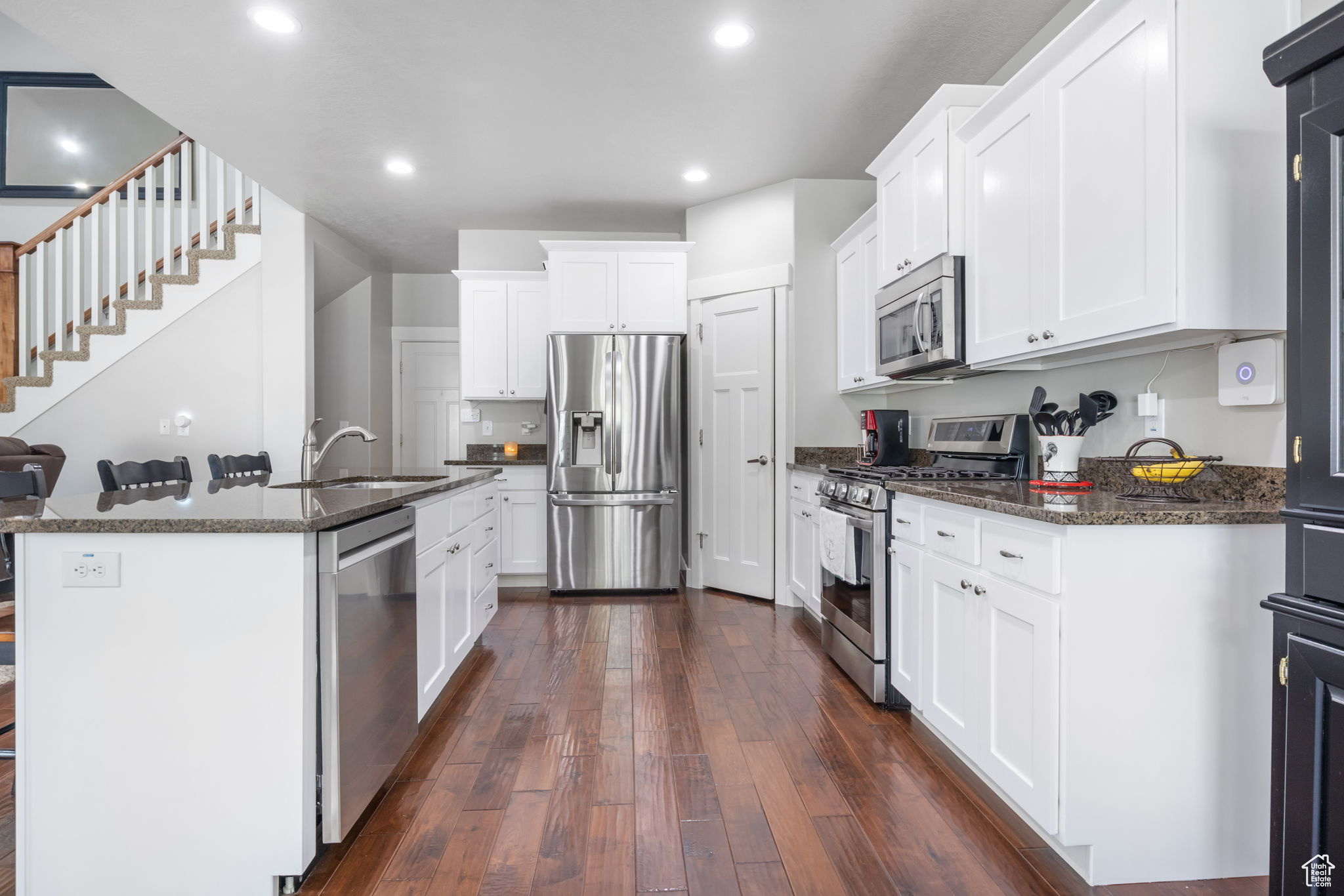 Kitchen featuring stainless steel appliances, dark wood-type flooring, sink, a center island with sink, and white cabinets