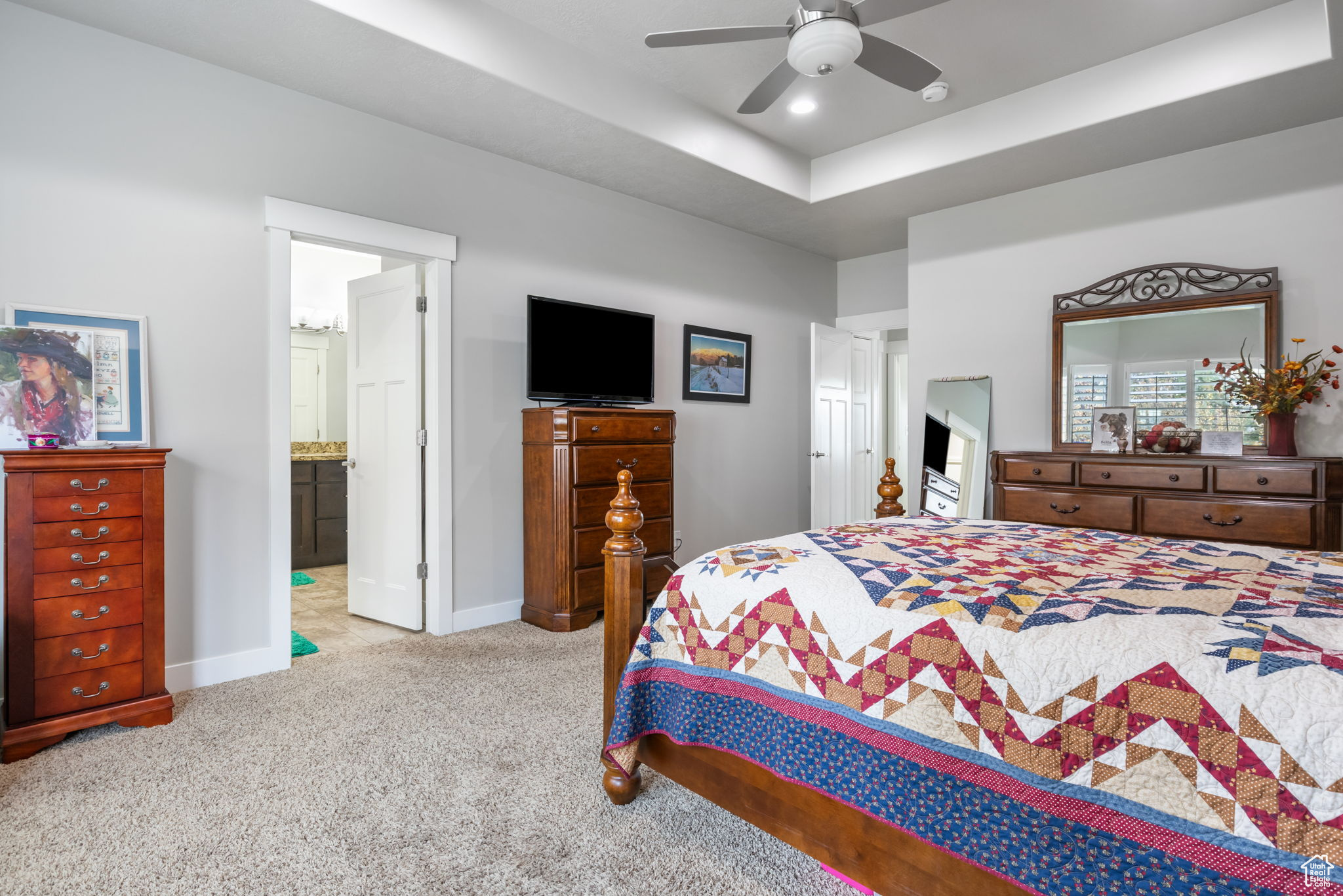 Carpeted bedroom with a raised ceiling, ensuite bathroom, and ceiling fan