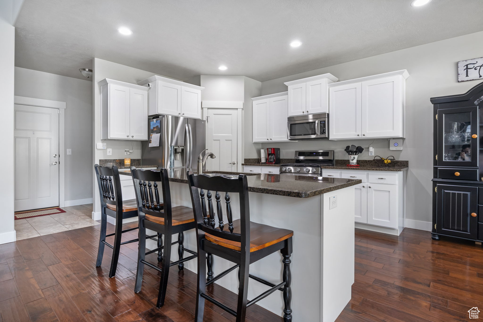 Kitchen with white cabinetry, an island with sink, dark wood-type flooring, and appliances with stainless steel finishes