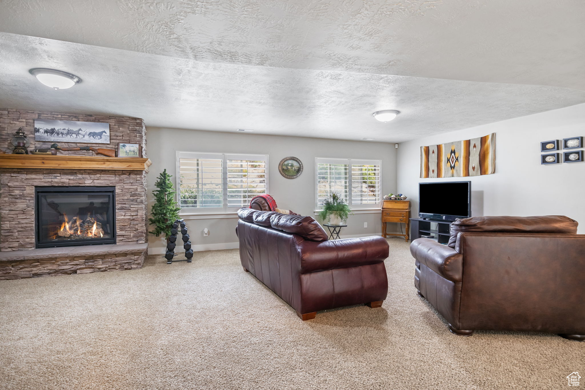 Living room with carpet, a textured ceiling, and a stone fireplace