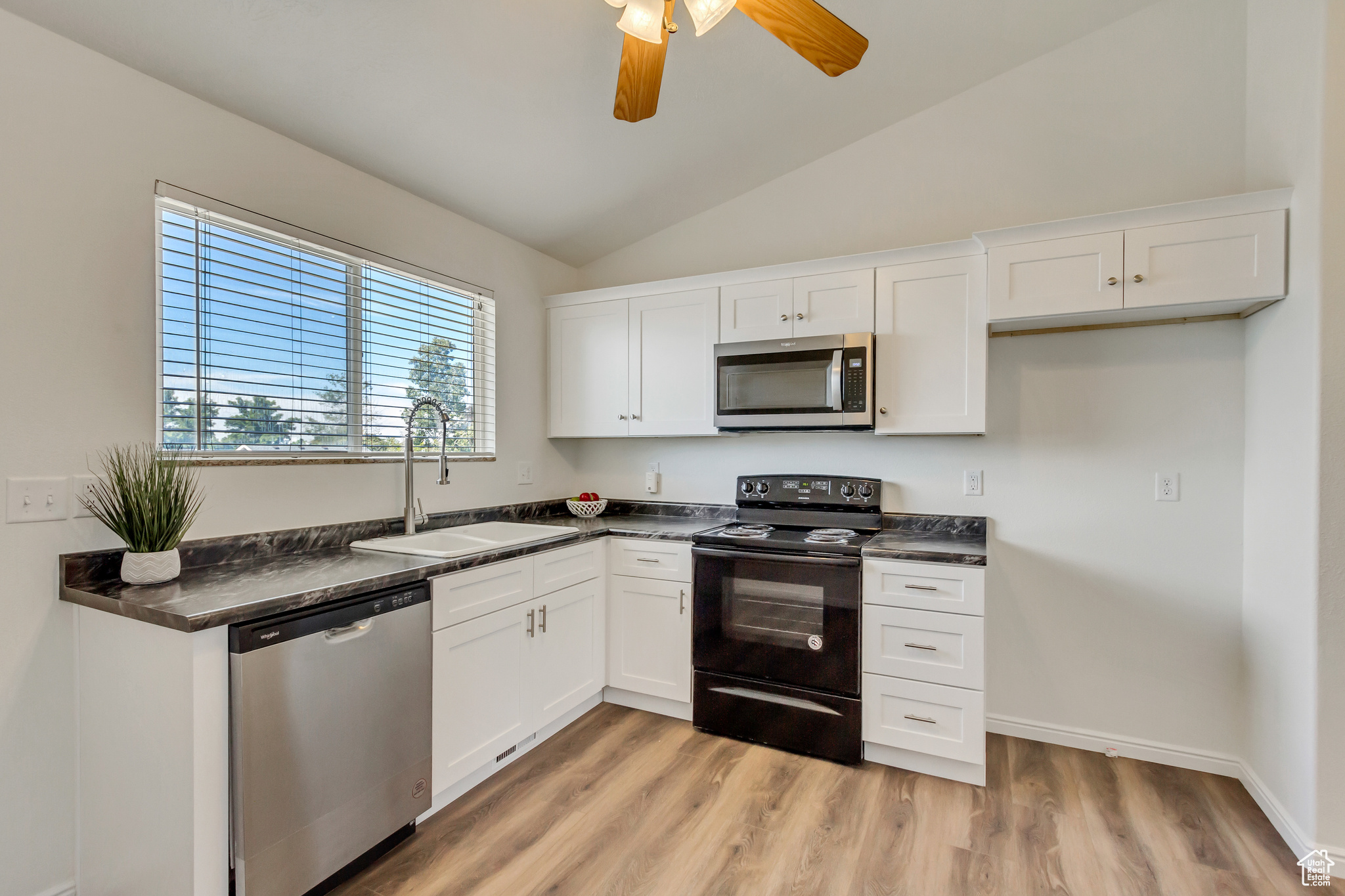 Kitchen featuring white cabinets, stainless steel appliances, lofted ceiling, and sink