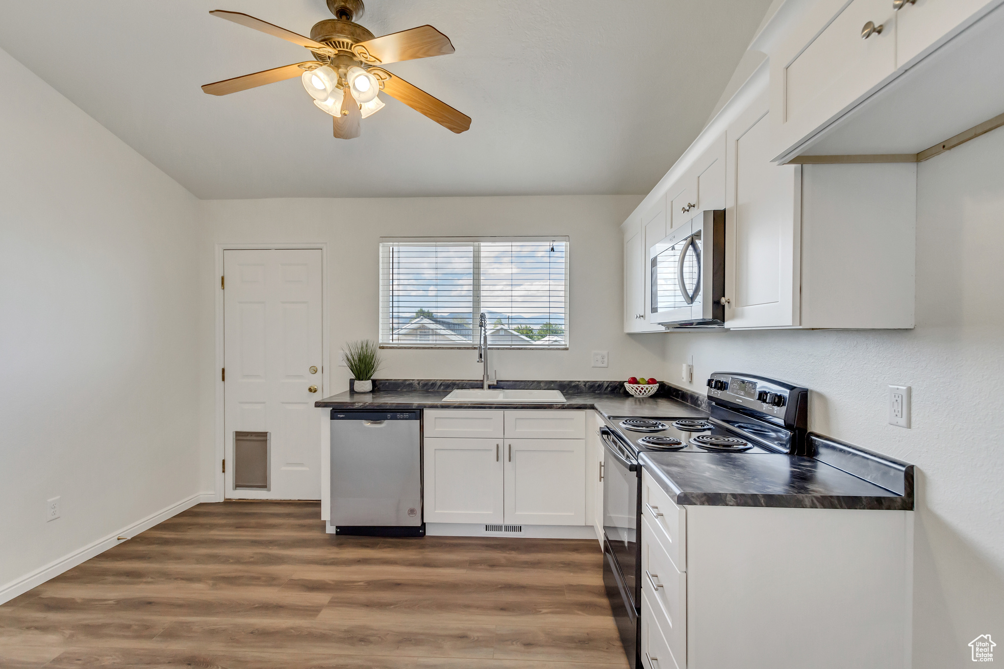 Kitchen with ceiling fan, sink, dark wood-type flooring, stainless steel appliances, and white cabinets