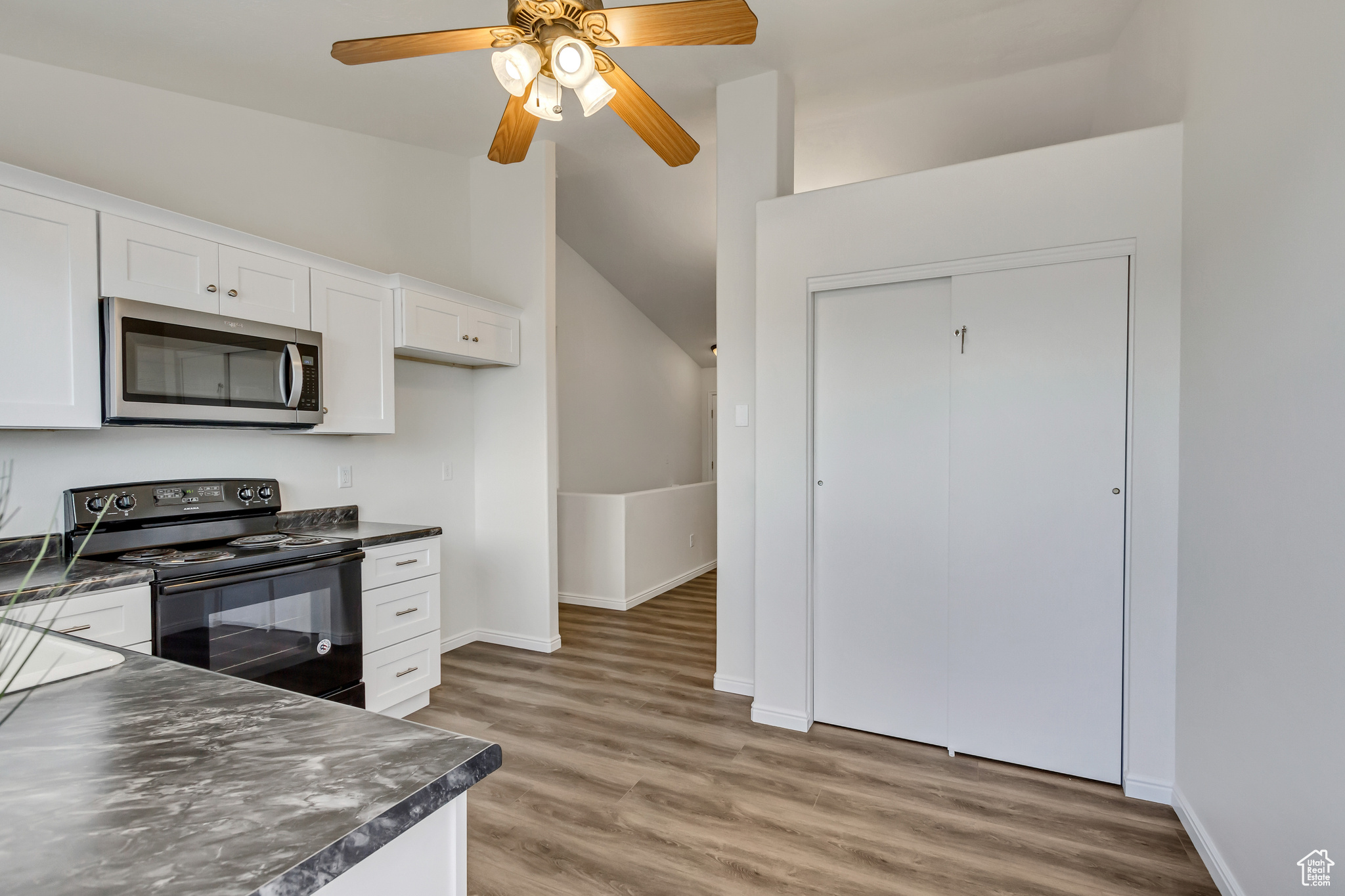 Kitchen featuring electric range, ceiling fan, lofted ceiling, white cabinets, and hardwood / wood-style flooring