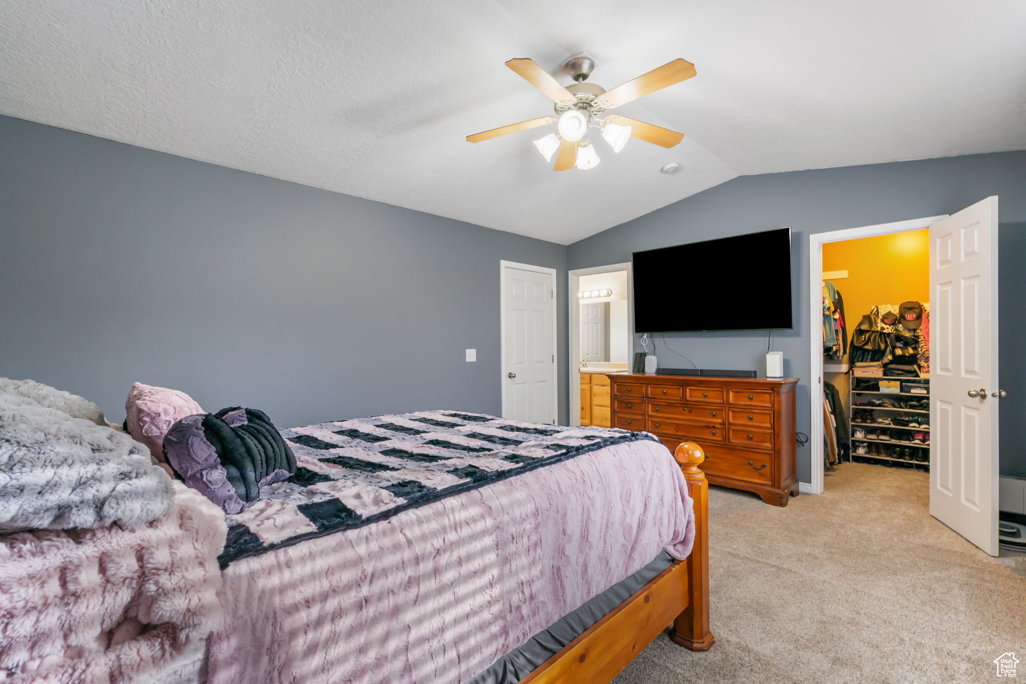 Bedroom with lofted ceiling, a walk in closet, ceiling fan, light colored carpet, and a closet