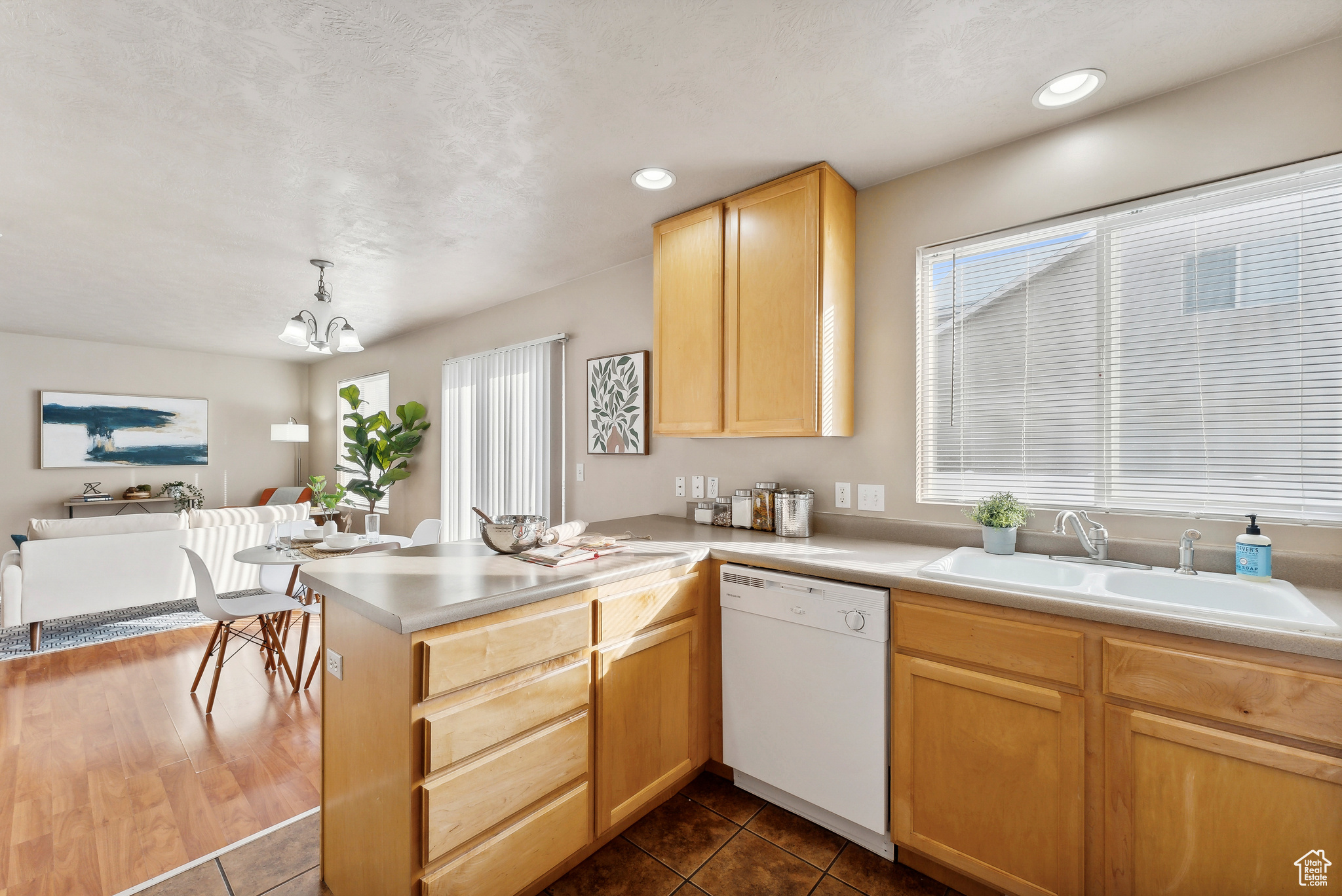 Kitchen featuring hanging light fixtures, kitchen peninsula, white dishwasher, light brown cabinetry, and dark tile patterned flooring