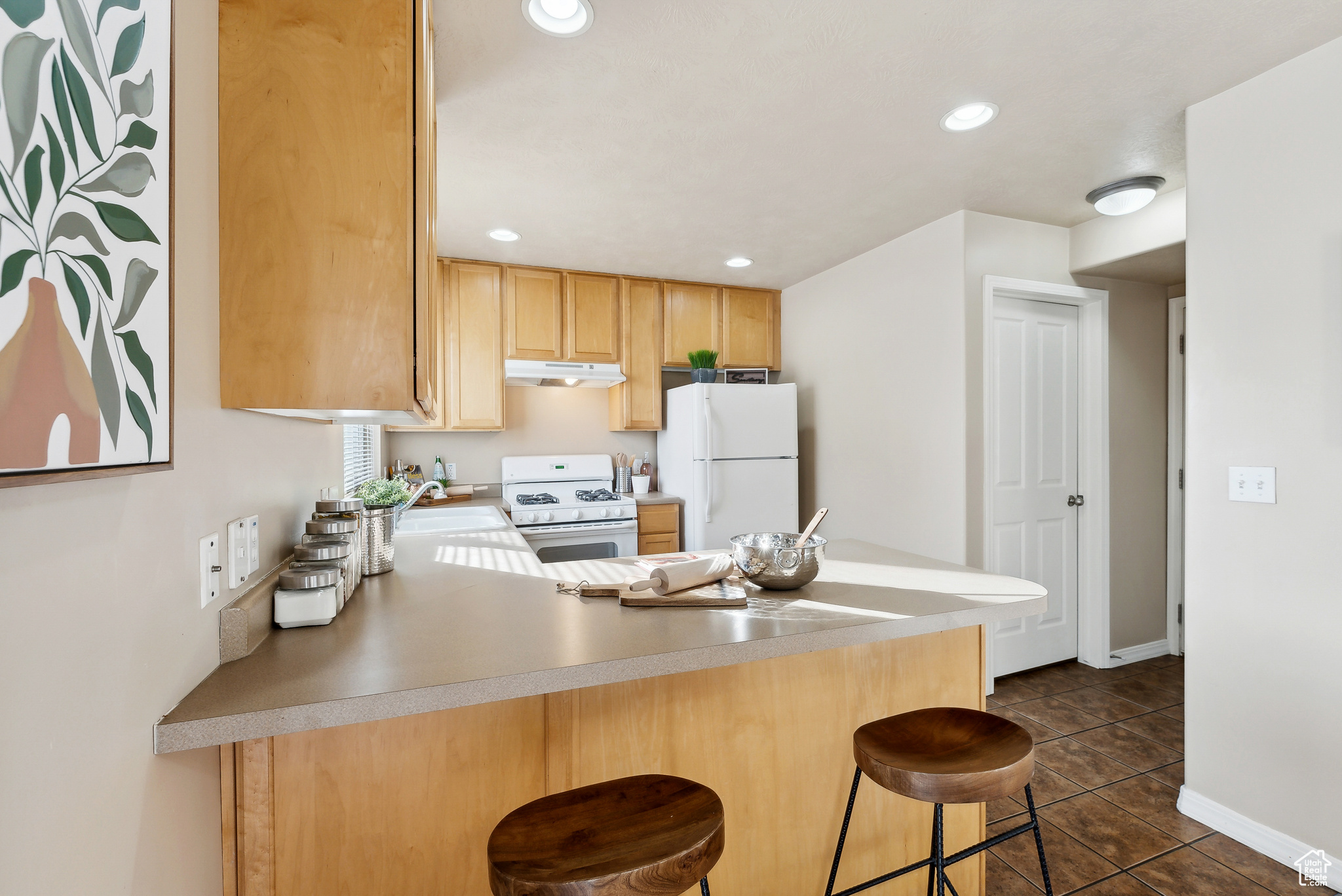 Kitchen with a breakfast bar, white appliances, dark tile patterned floors, sink, and light brown cabinets