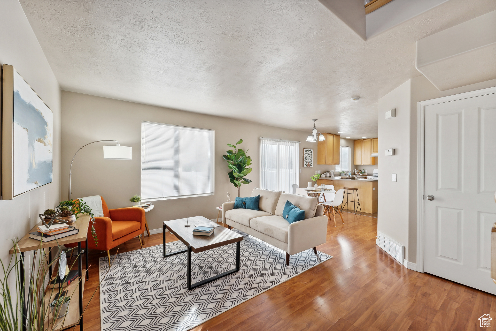 Living room with light wood-type flooring, a textured ceiling, and an inviting chandelier