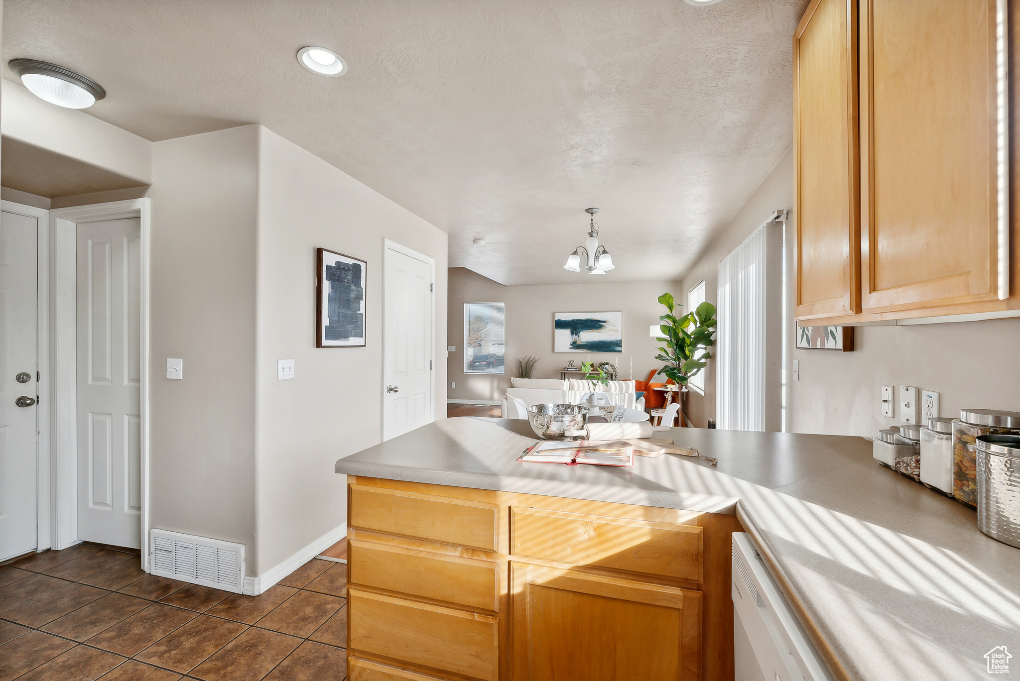 Kitchen featuring a healthy amount of sunlight, dark tile patterned floors, light brown cabinetry, and an inviting chandelier