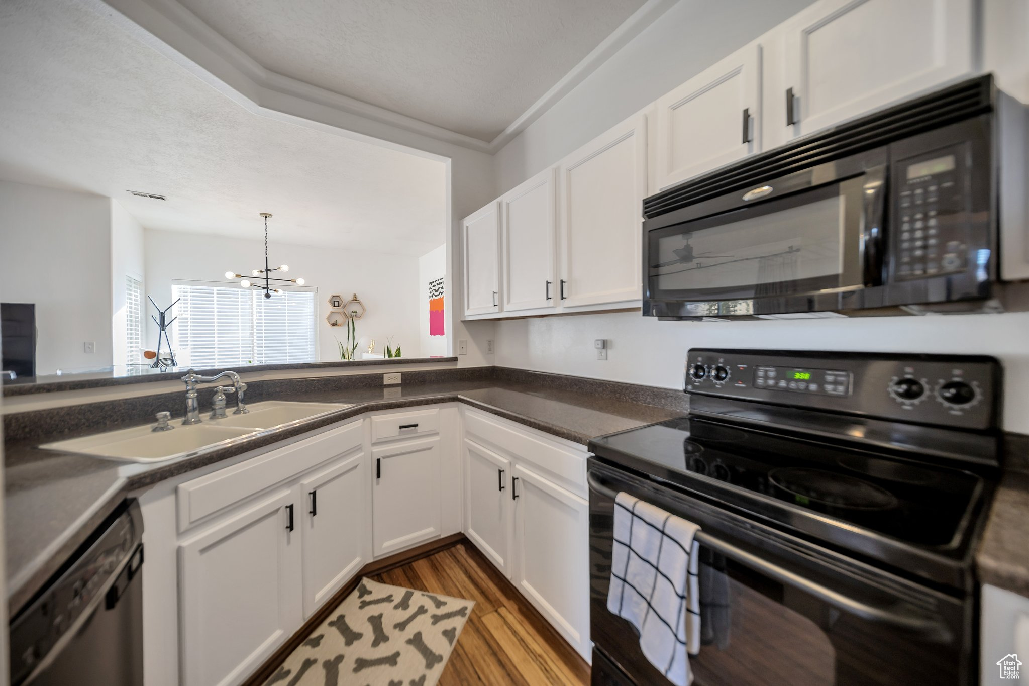 Kitchen with ornamental molding, sink, black appliances, an inviting chandelier, and white cabinetry