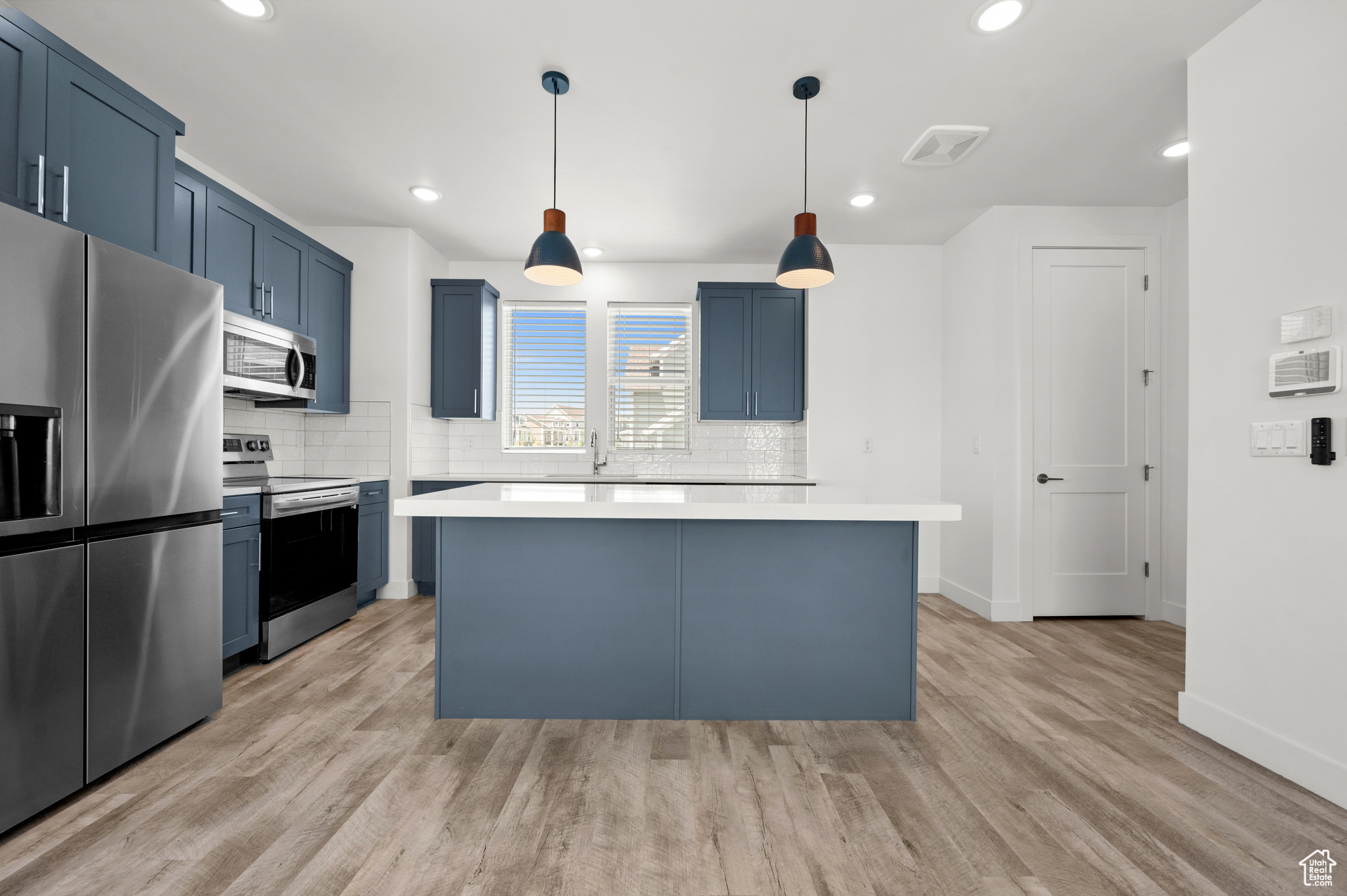 Kitchen with light hardwood / wood-style floors, a kitchen island, stainless steel appliances, and hanging light fixtures