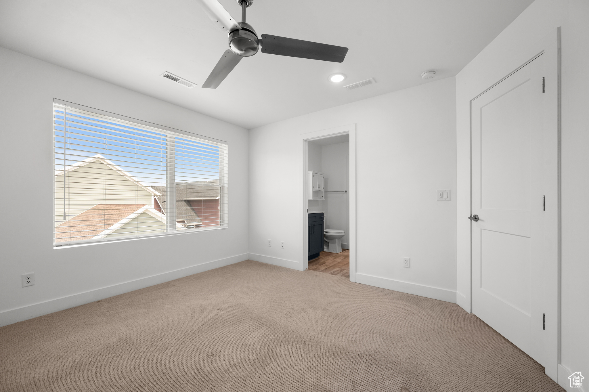 Unfurnished bedroom with connected bathroom, ceiling fan, and light colored carpet