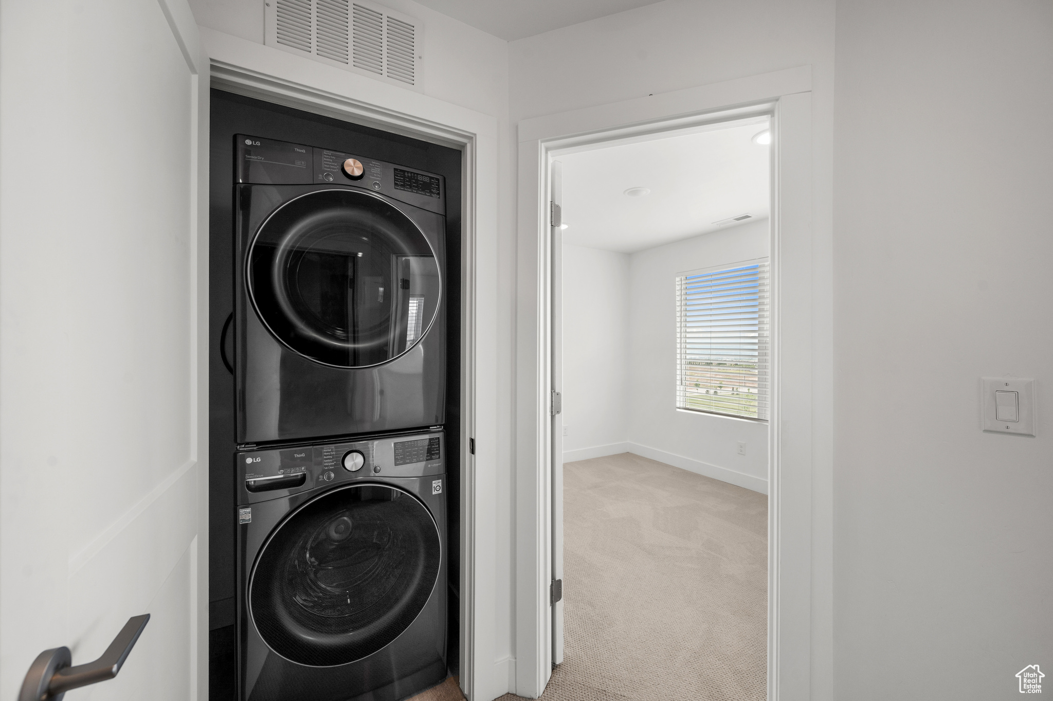 Clothes washing area featuring light carpet and stacked washer and dryer