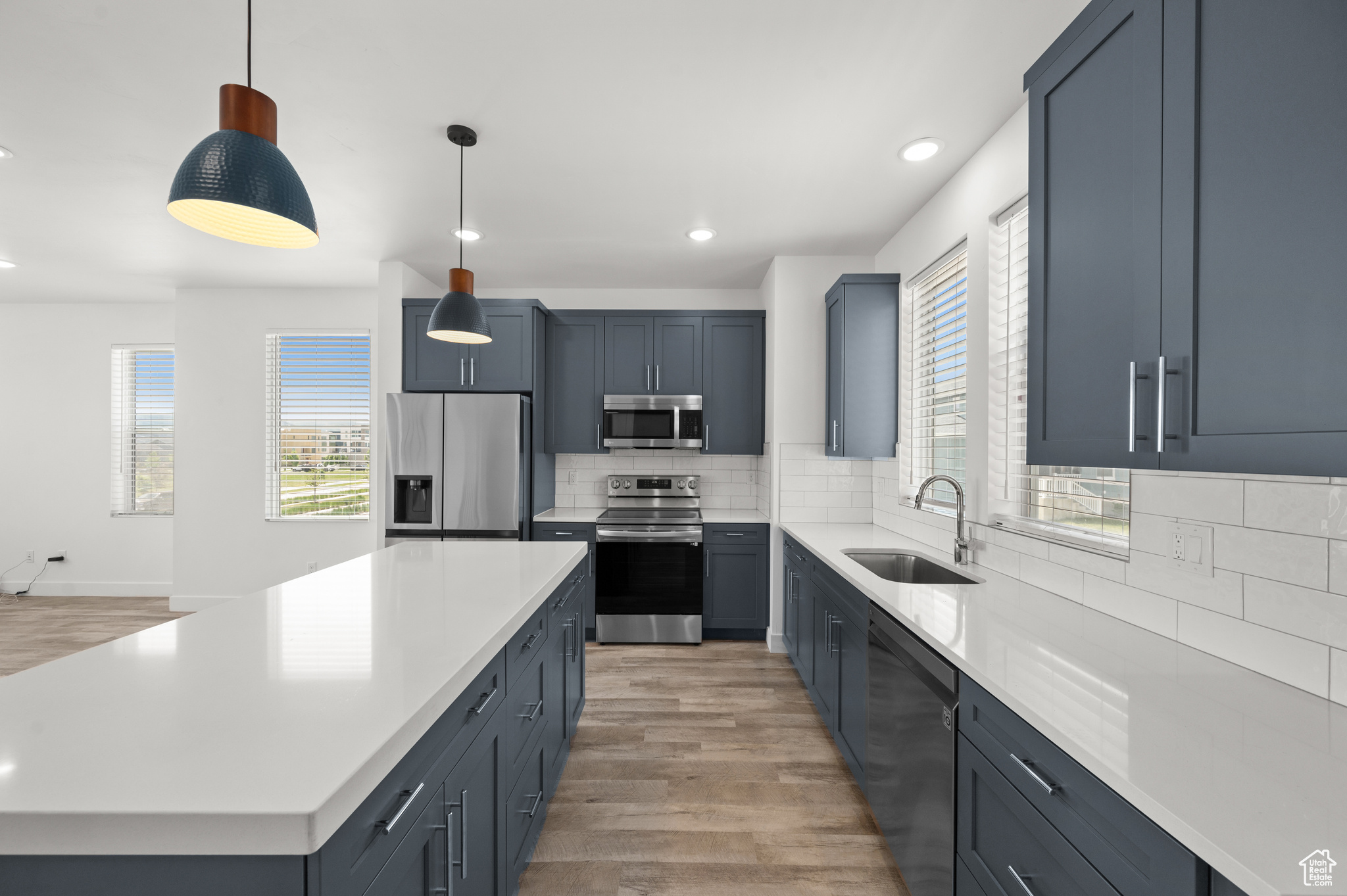 Kitchen with sink, hanging light fixtures, stainless steel appliances, decorative backsplash, and light wood-type flooring