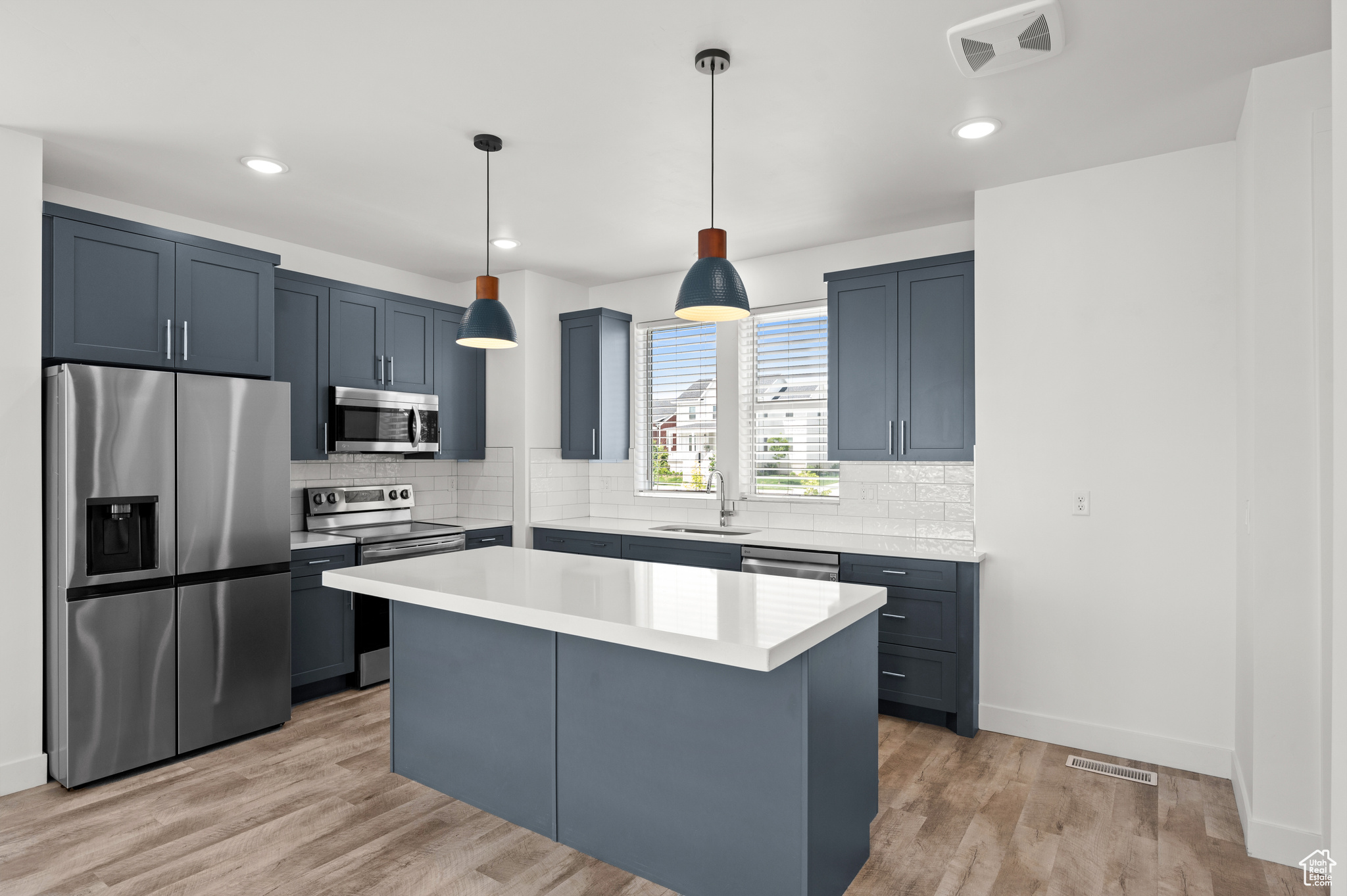 Kitchen with appliances with stainless steel finishes, sink, light hardwood / wood-style flooring, a center island, and hanging light fixtures