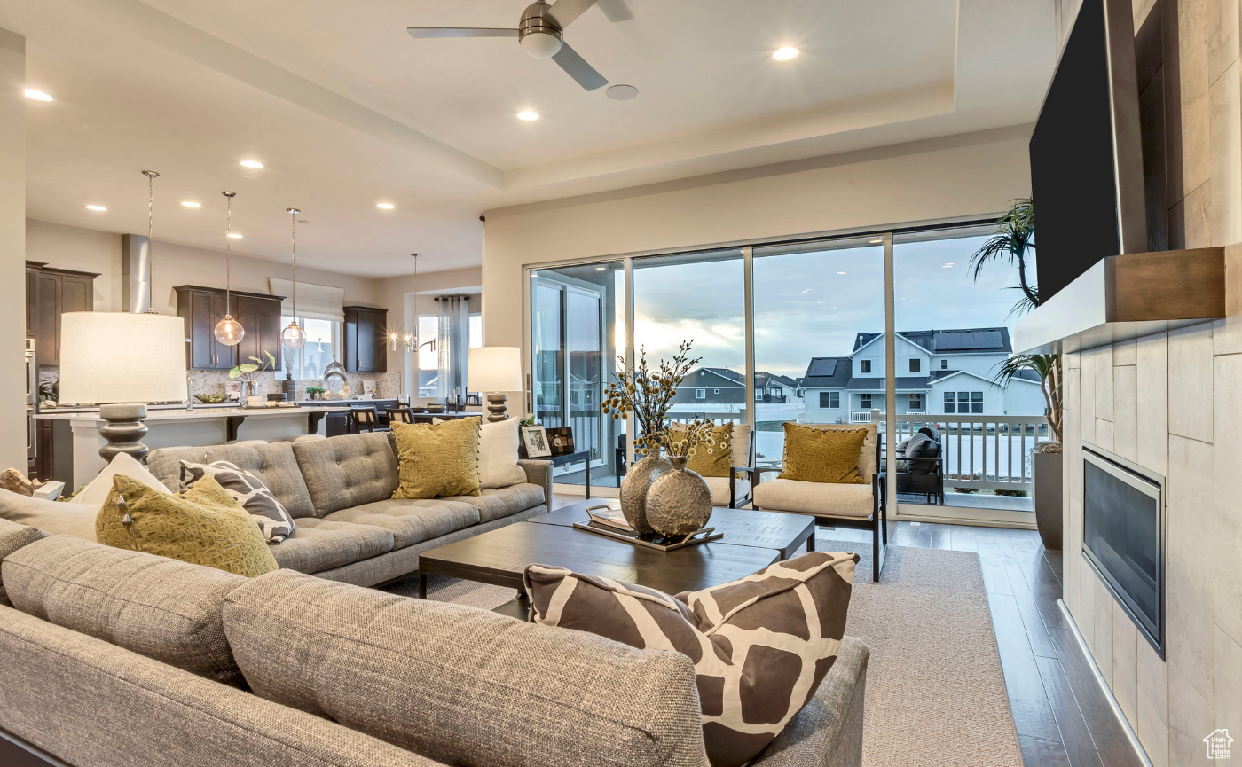 Living room featuring a tray ceiling, a tiled fireplace, ceiling fan, and hardwood / wood-style floors