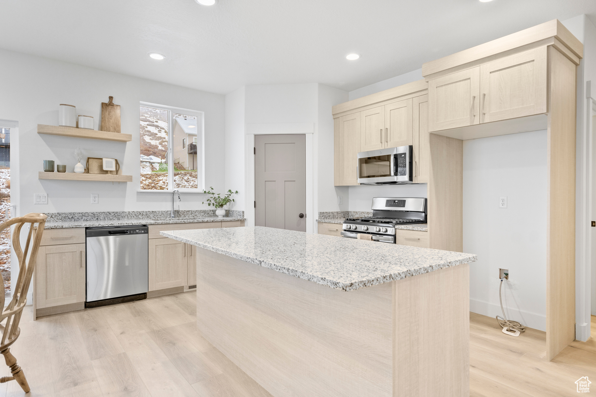 Kitchen featuring light stone countertops, appliances with stainless steel finishes, sink, a center island, and light hardwood / wood-style floors