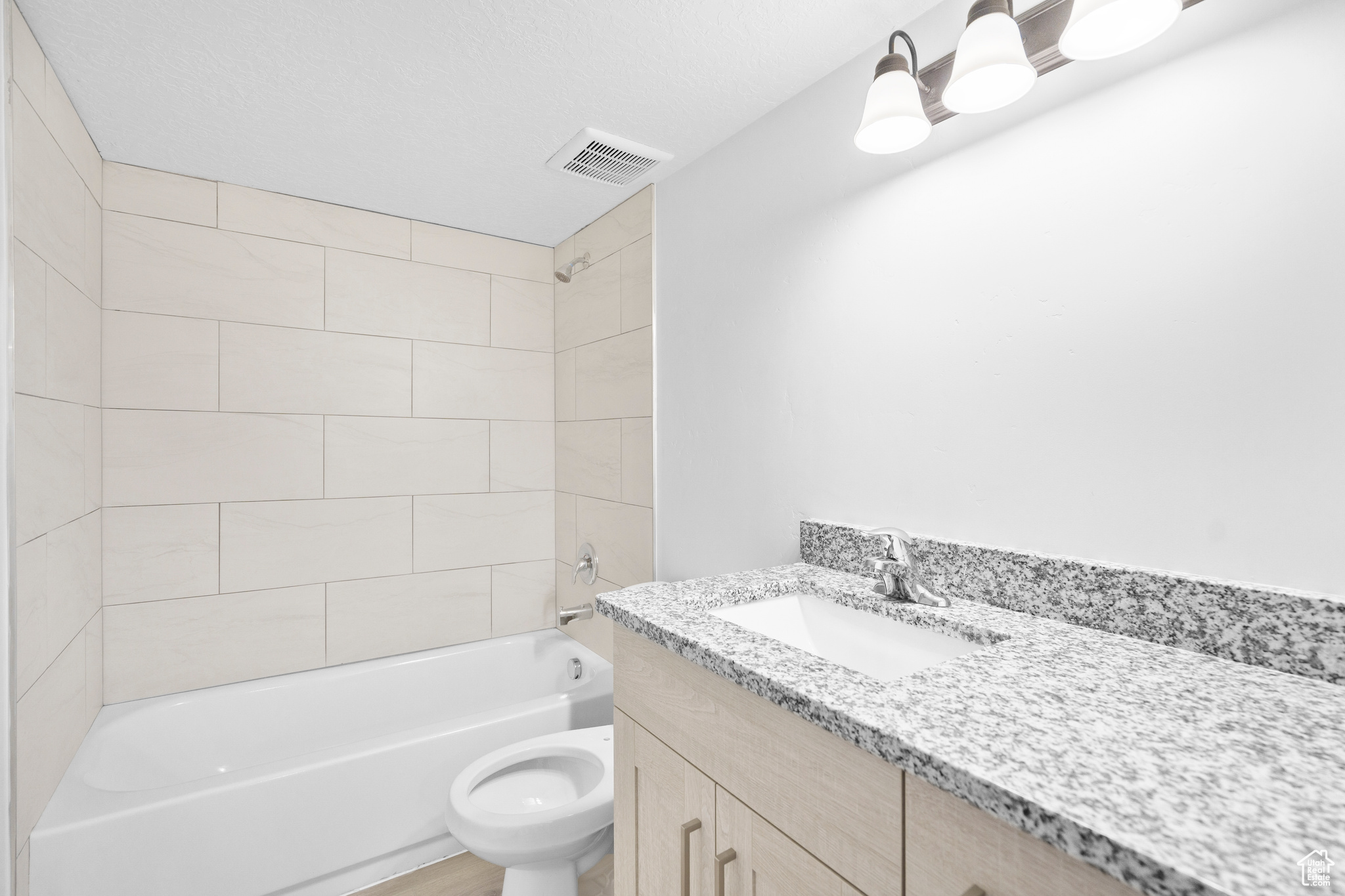 Full bathroom with tiled shower / bath, vanity, a textured ceiling, and toilet