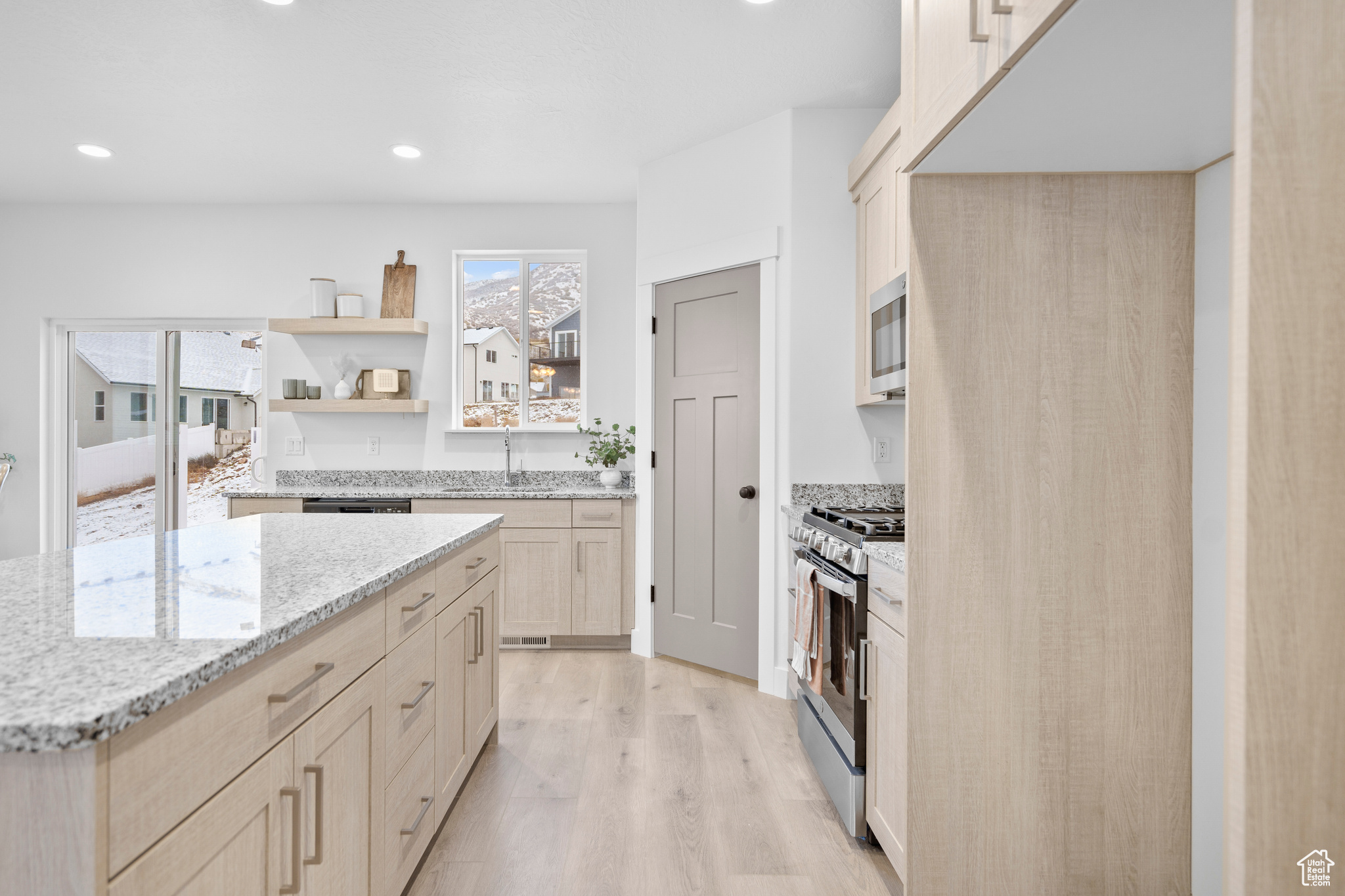 Kitchen with light stone countertops, appliances with stainless steel finishes, light brown cabinetry, sink, and light hardwood / wood-style flooring