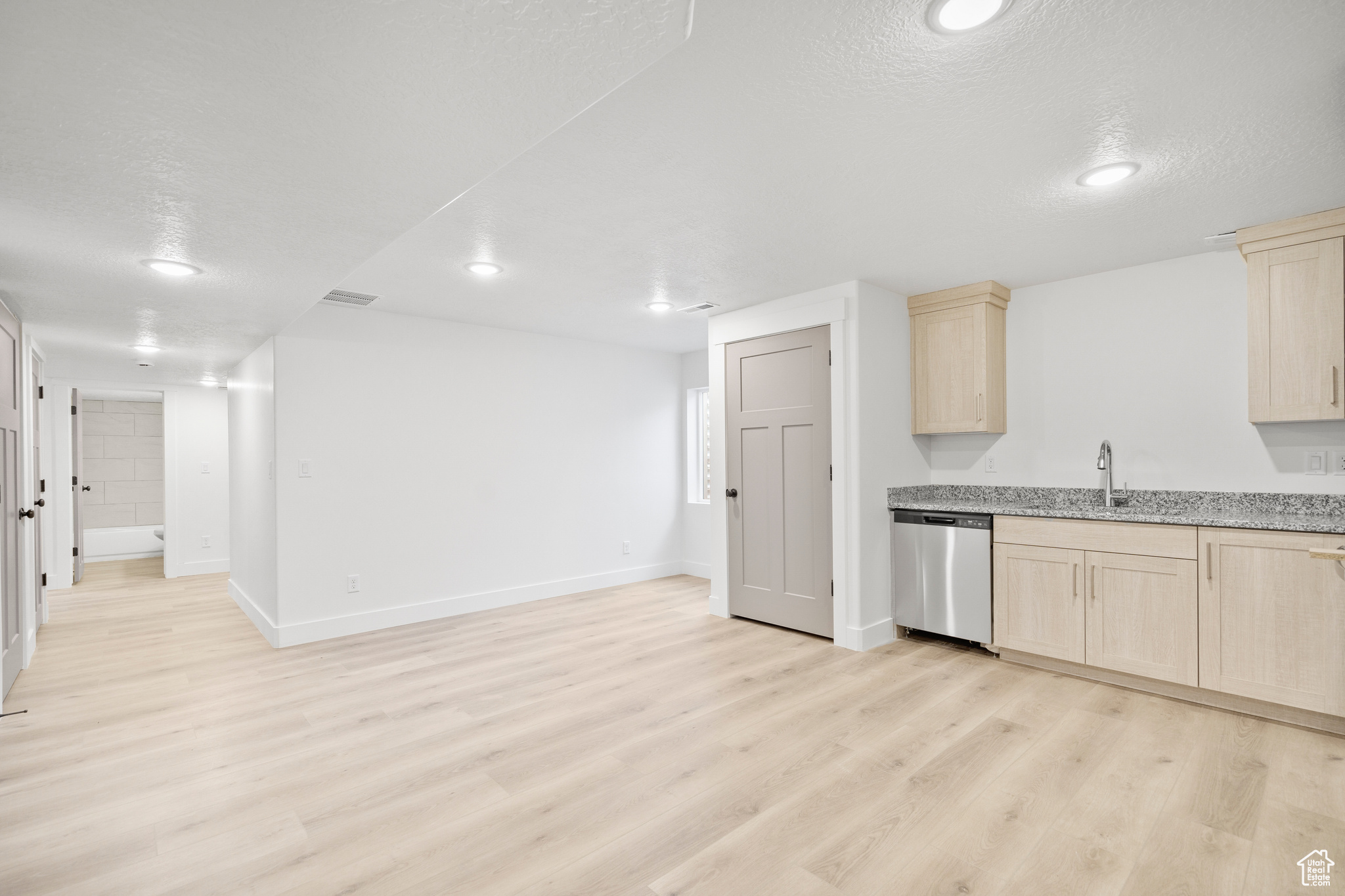 Kitchen with stainless steel dishwasher, a textured ceiling, sink, light brown cabinets, and light hardwood / wood-style floors