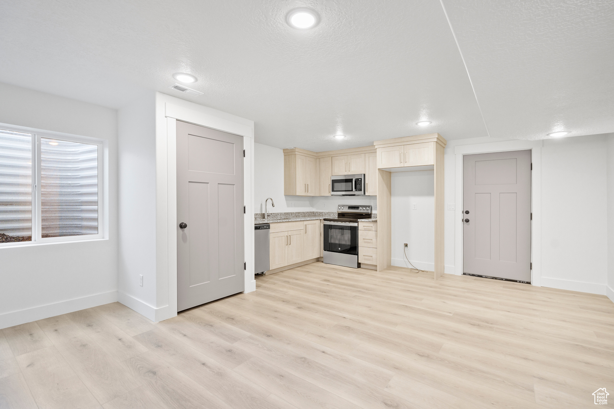 Kitchen with cream cabinets, sink, a textured ceiling, light hardwood / wood-style floors, and stainless steel appliances