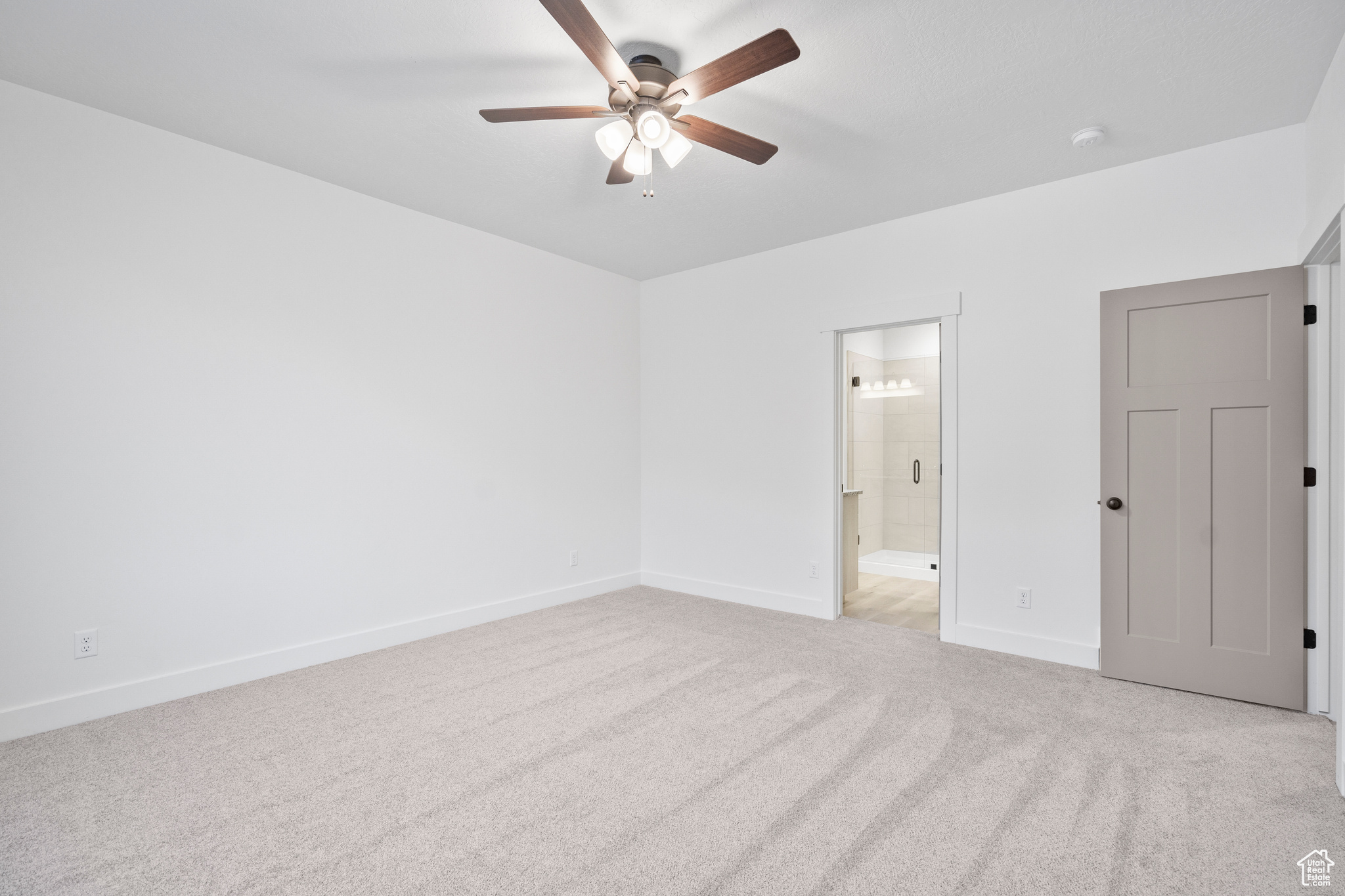 Unfurnished bedroom with ceiling fan, ensuite bathroom, and light carpet