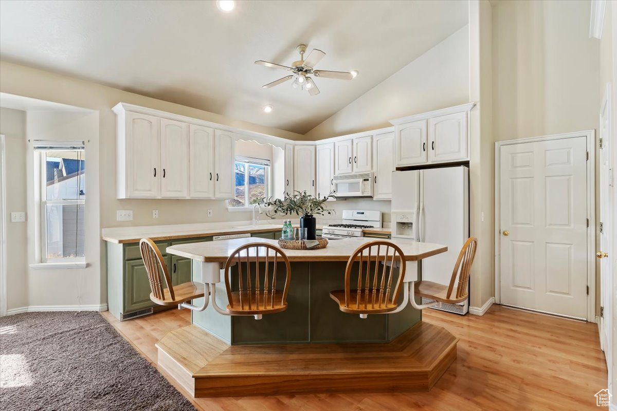 Kitchen with white appliances, a kitchen island, ceiling fan, light hardwood / wood-style flooring, and white cabinetry