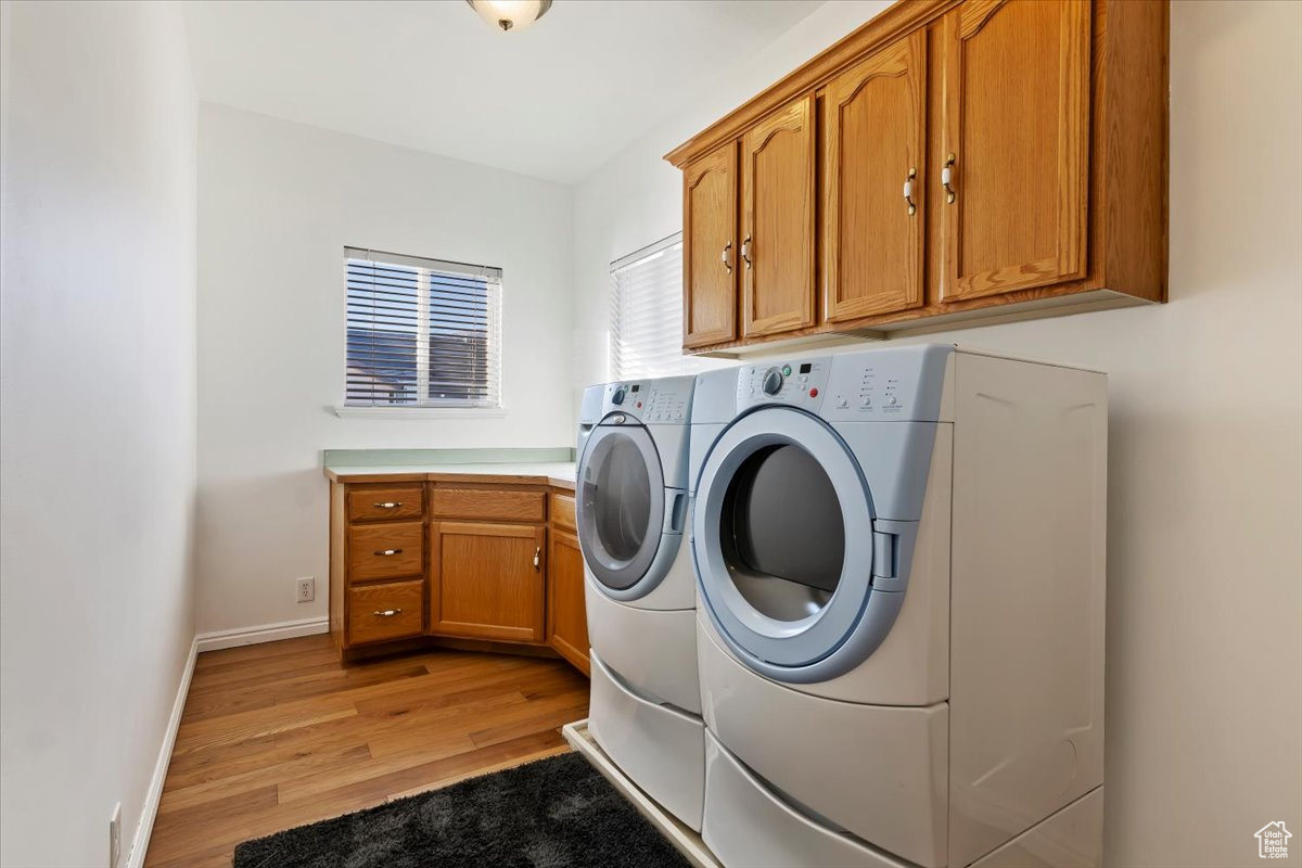 Laundry area featuring separate washer and dryer, cabinets, and light hardwood / wood-style floors