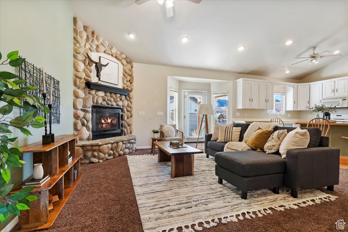 Carpeted living room featuring ceiling fan, a fireplace, and vaulted ceiling