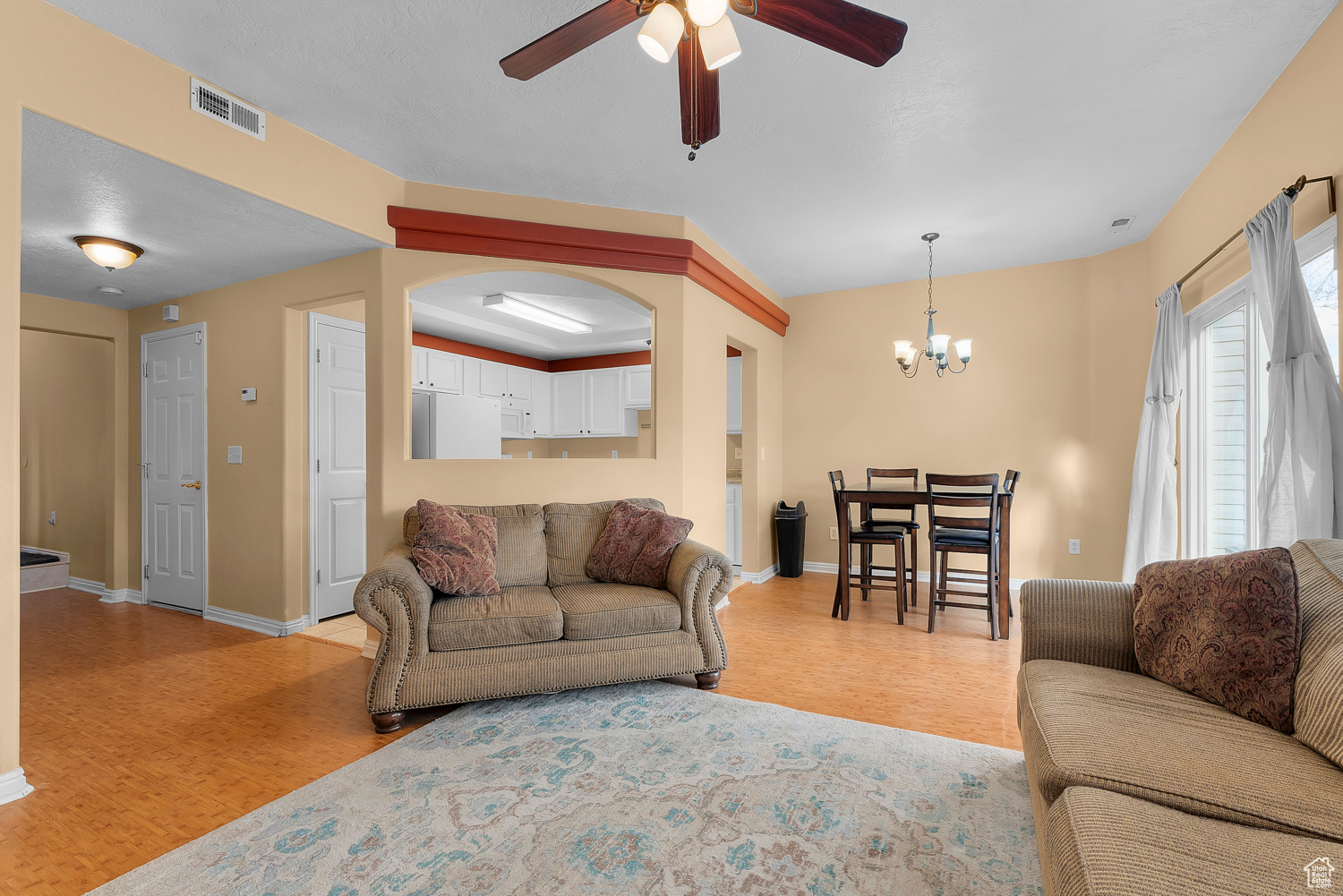 Living room with light parquet flooring and ceiling fan with notable chandelier